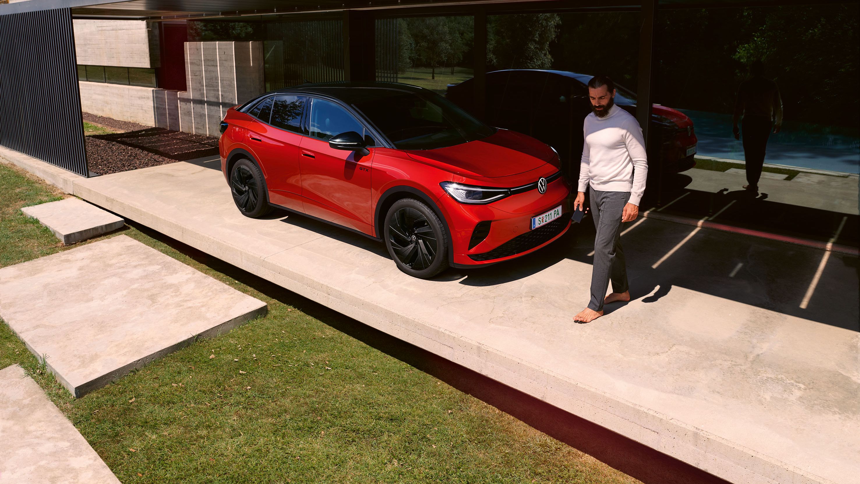 Červené VW ID.5 GTX parkuje pred domom. Muž prechádza okolo neho.