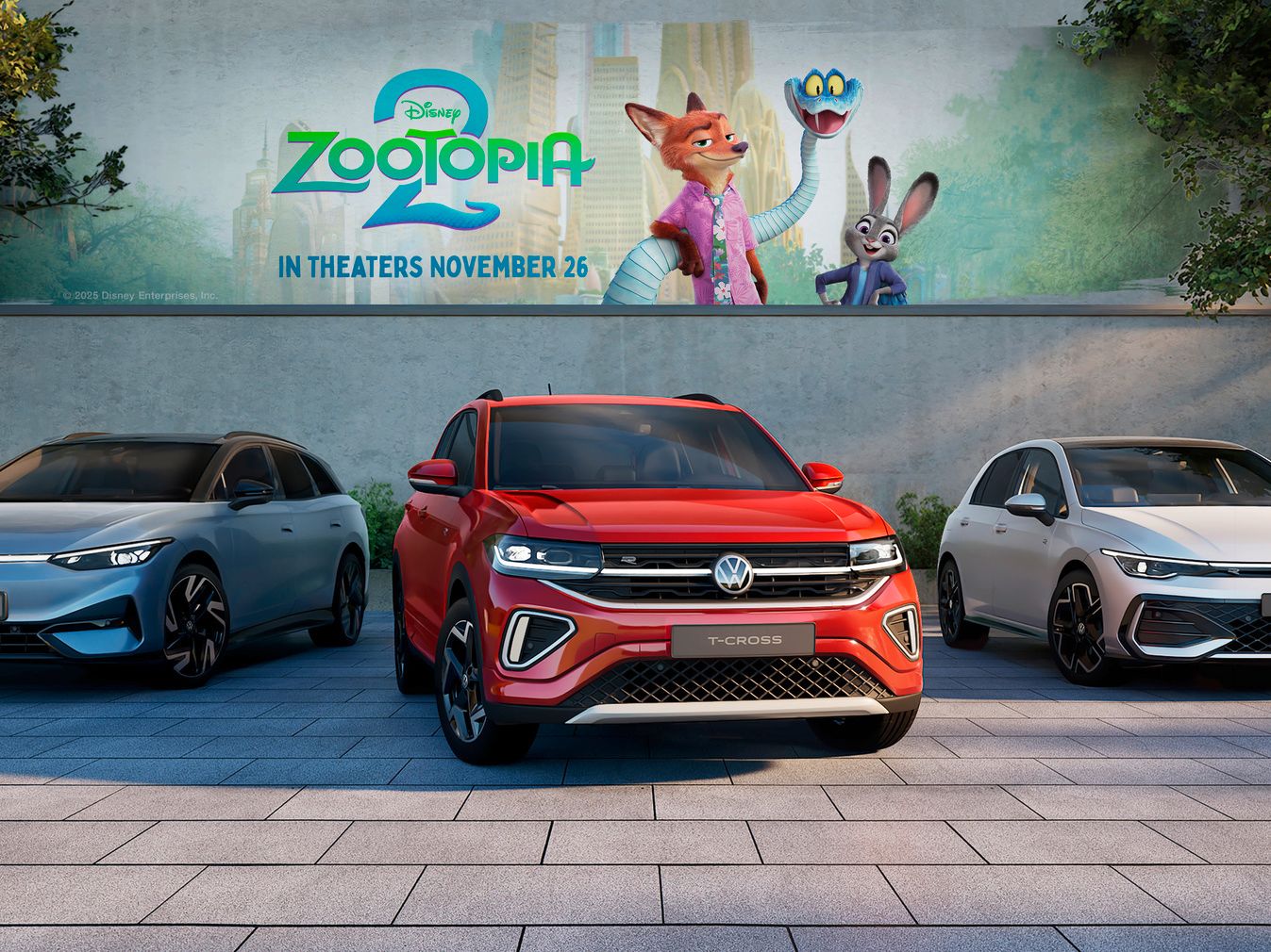 Tri modely automobilov Volkswagen (ID.4X, T-Cross a Golf) zaparkované pred billboardom s filmom Zootopia 2. V pozadí sú stromy a zeleň. Automobily sú rôznych farieb: modrá, červená a biela.