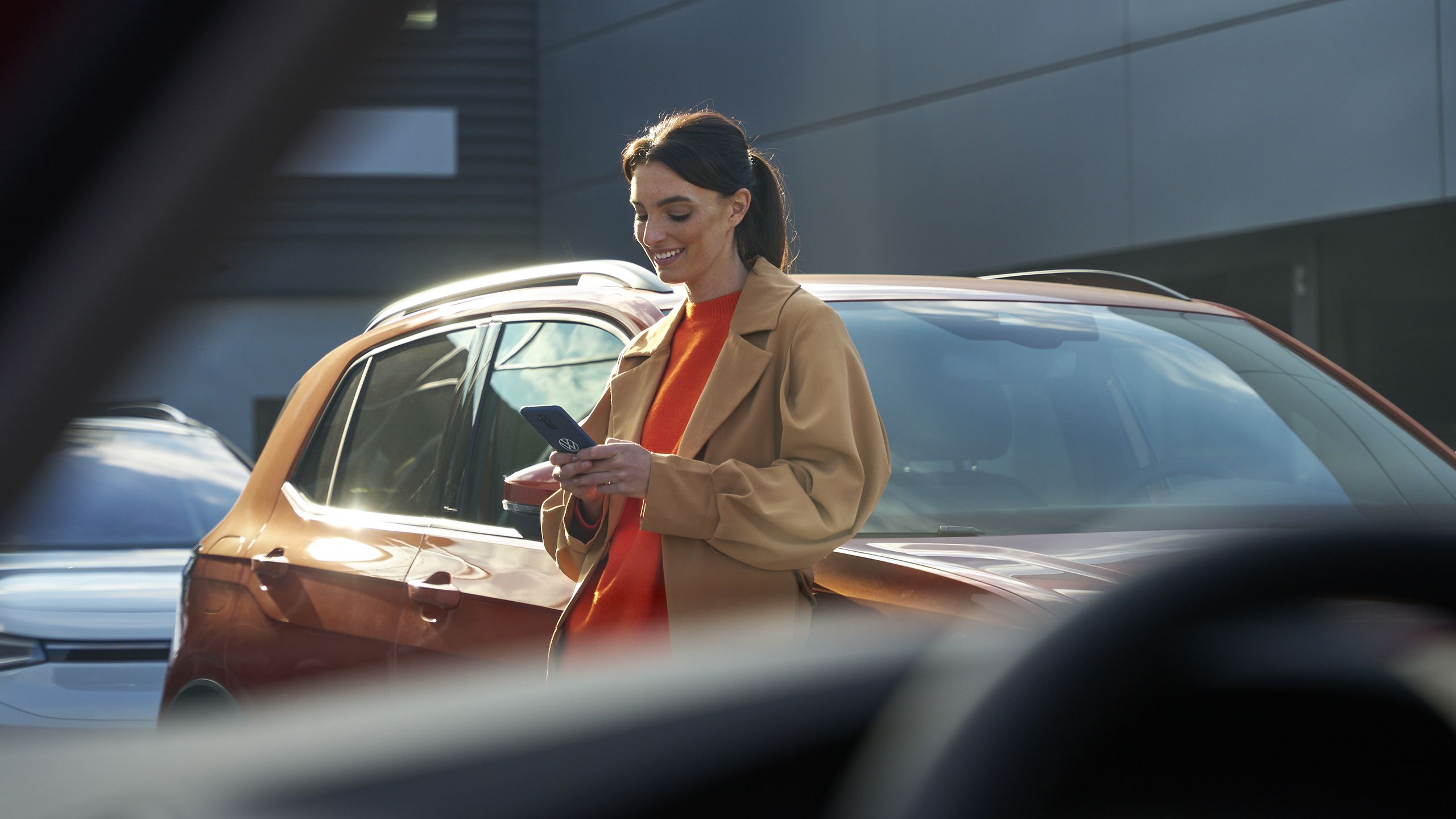 Žena sa opiera o auto VW a používa zákaznícke centrum na svojom smartfóne.