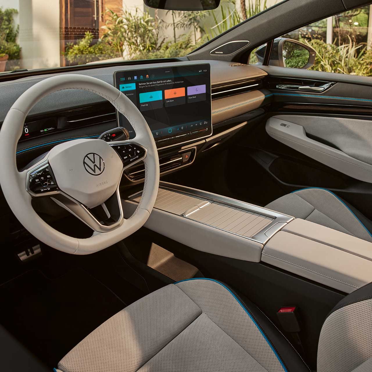 Interiér moderného automobilu značky Volkswagen s čiernym a svetlo sivým čalúnením. Na palubnej doske je veľký dotykový displej. V popredí je svetlo sivý volant s logom VW.