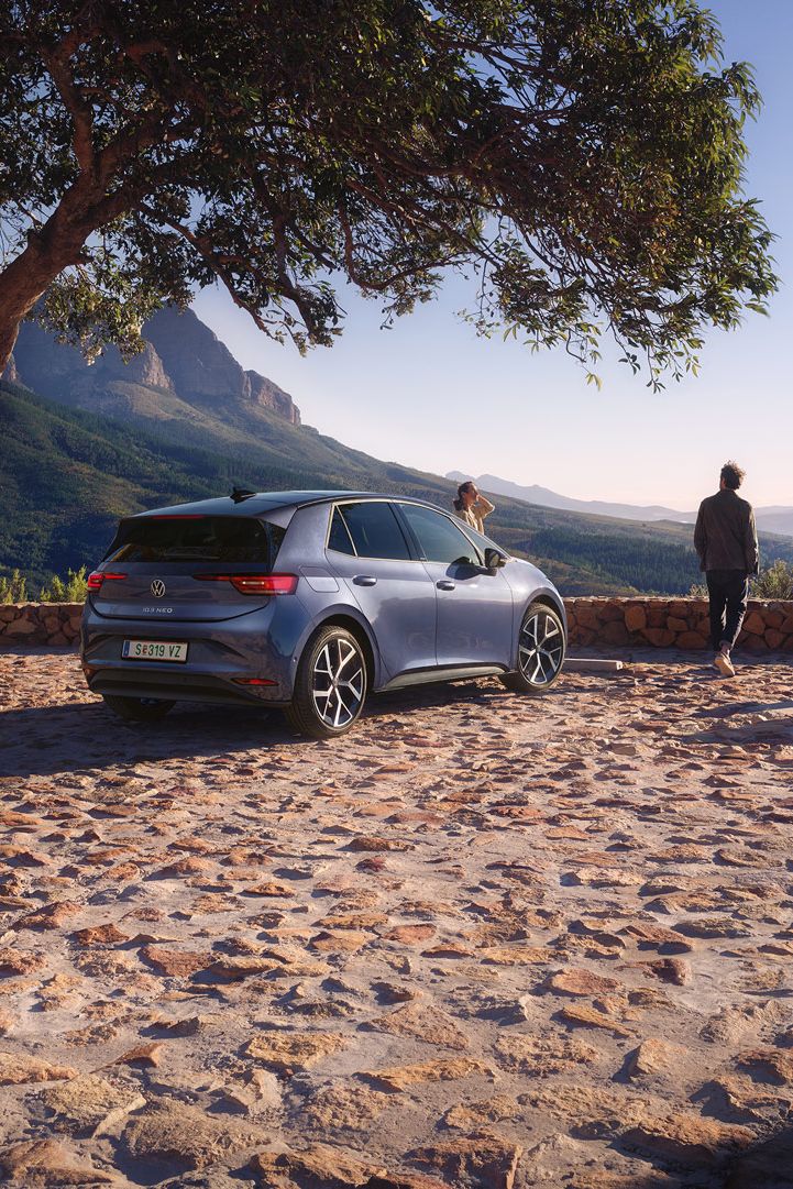 Na parkovisku v horách stojí modrý VW ID.3 Neo, žena a muž si užívajú výhľad.