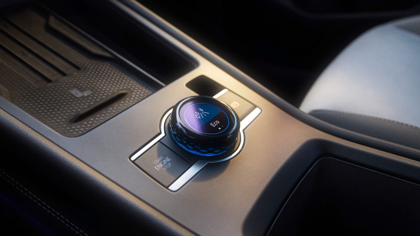Detailný záber stredovej konzoly v modeli T-Roc so zameraním na prepínač jazdných režimov. Okrúhle otočné tlačidlo s LED ukazovateľmi na ovládanie rôznych funkcií vozidla. Viditeľné sú vysokokvalitné materiály a elegantný dizajn.