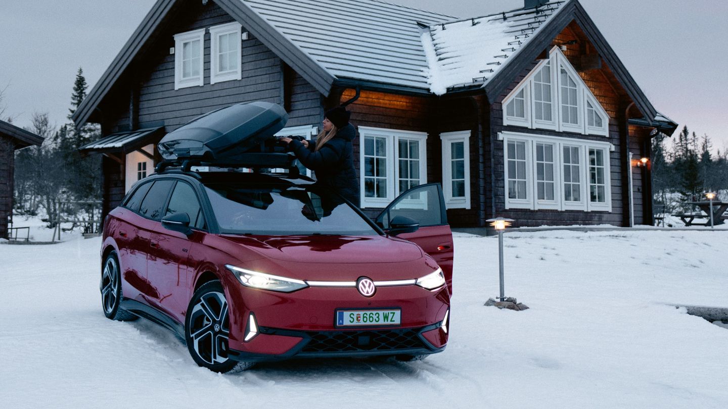 Červený ID.7 Tourer GTX so strešným boxom stojí v snehu pred domom.