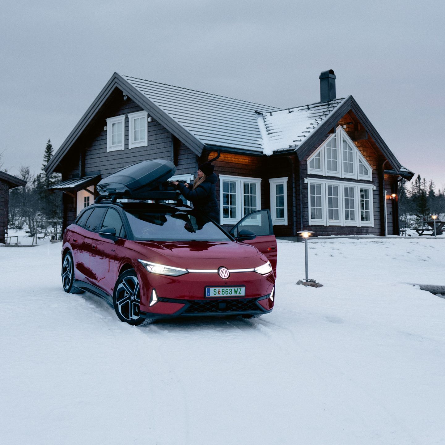 Červený ID.7 Tourer GTX so strešným boxom stojí v snehu pred domom.