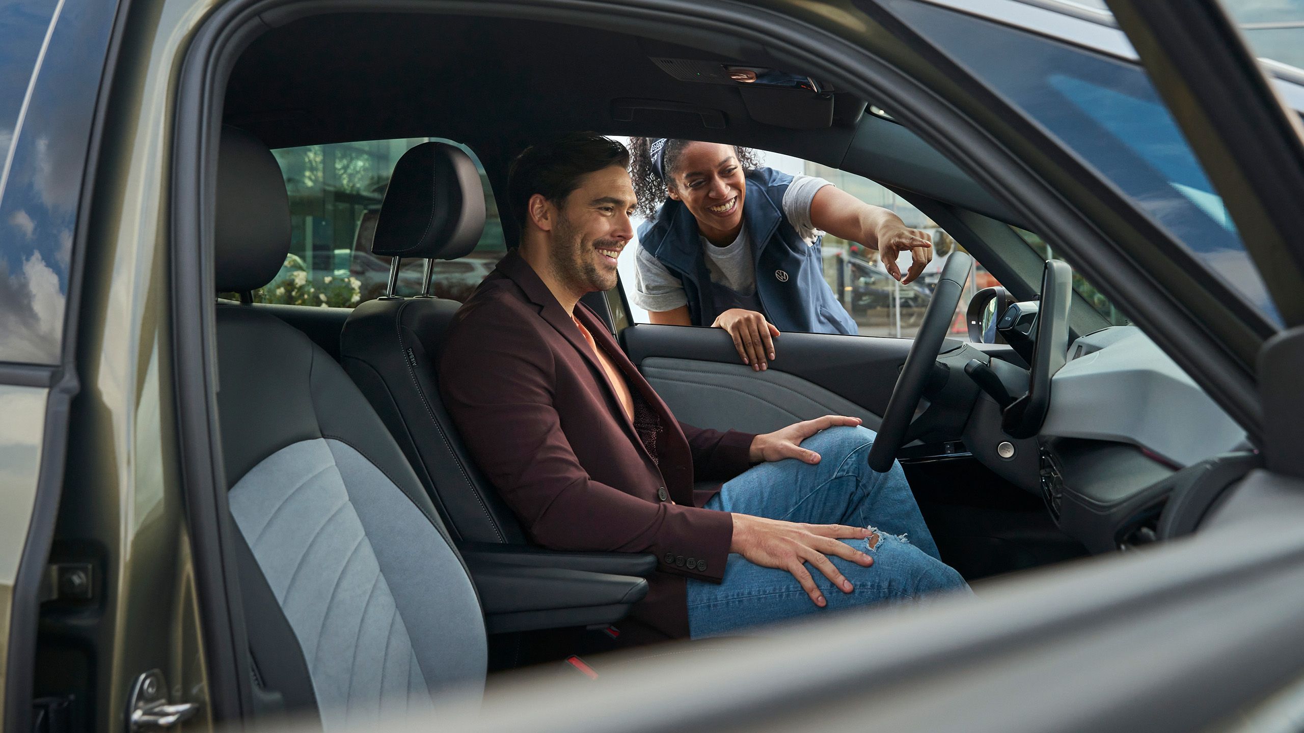 VW-Servicemitarbeiter zeigt einem Kunden etwas im Fahrzeug, Kunde sitzt im Auto