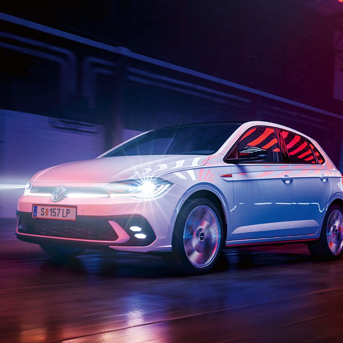 Biely VW Polo GTI jazdí v hale so zapnutými Matrix LED svetlometmi a svetelným pásom vpredu.