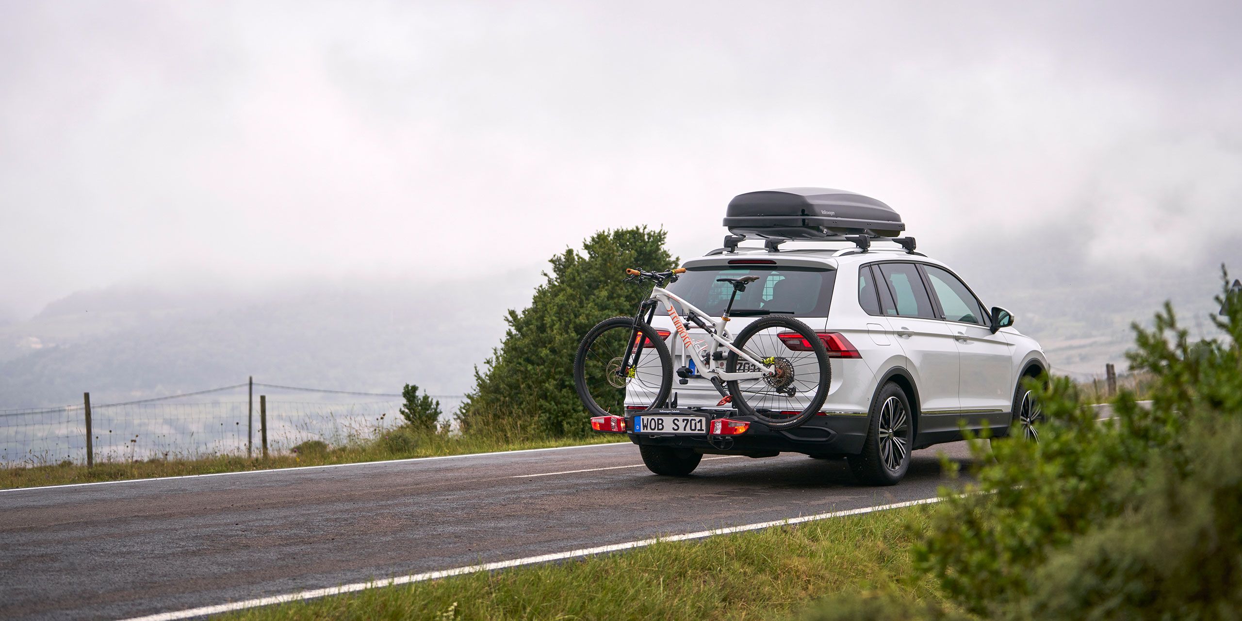 VW Tiguan so strešným boxom a nosičom bicyklov z originálneho príslušenstva Volkswagen vrátane bicykla na poľnej ceste