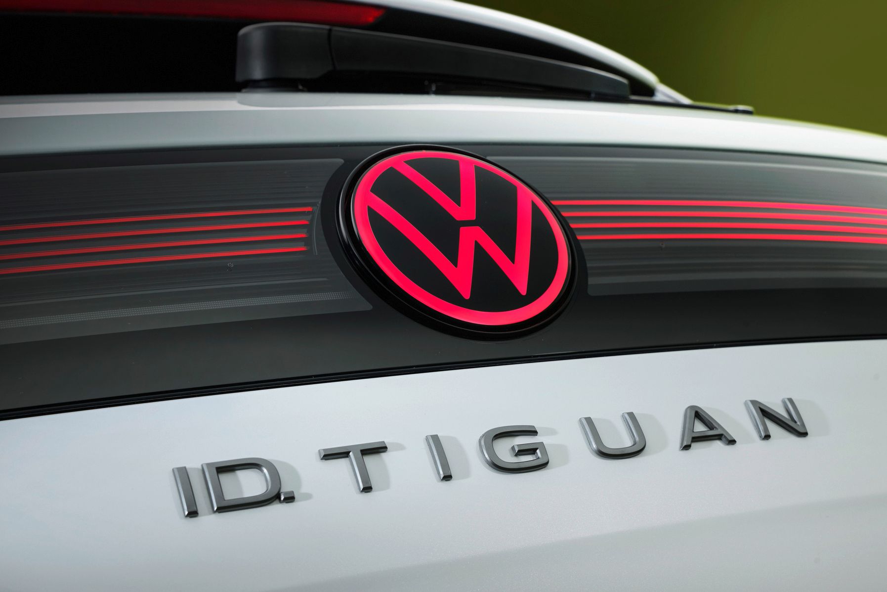 Detailný pohľad na osvetlené logo VW a názov modelu ID. Tiguan na zadných dverách bieleho vozidla.