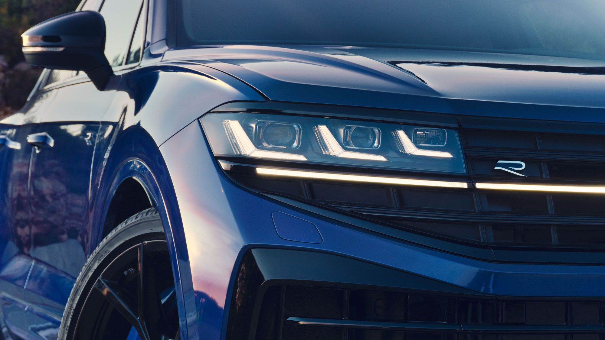 Detailný pohľad predné partie VW Touareg R eHybrid zameraný na dizajnový disk kolesa a Matrix LED svetlomet. Na mriežke chladiča je logo R.