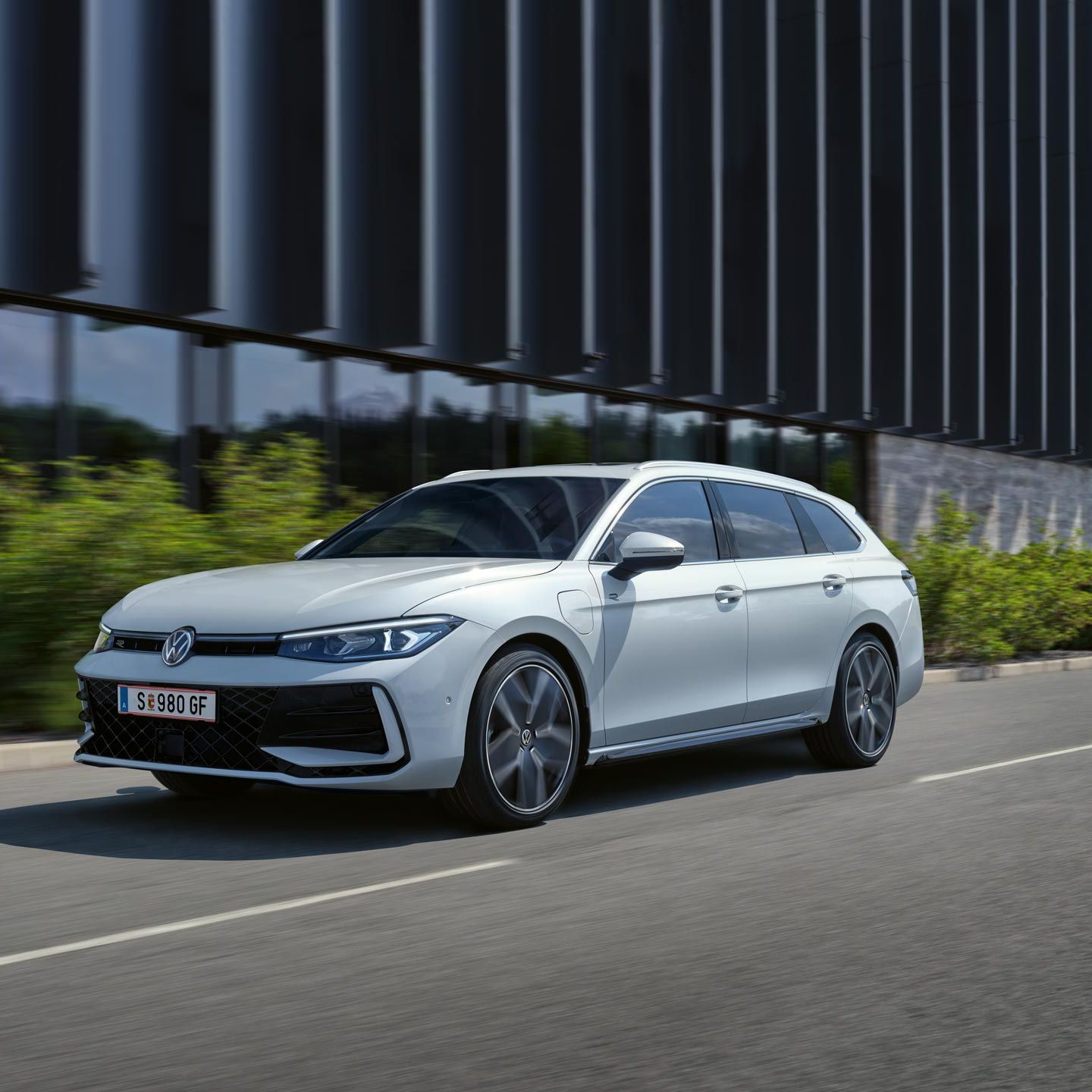Okolo budovy prechádza biely VW Passat s riadenými tlmičmi a dynamickým riadením.