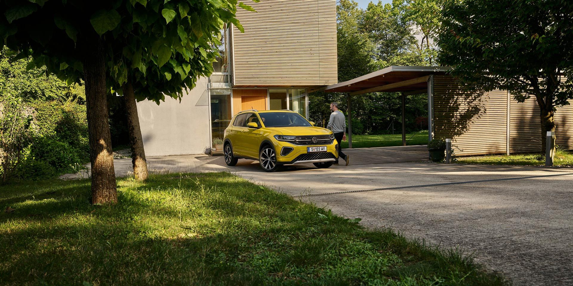 Muž sa chystá nastúpiť do žltého VW T-Cross, ktoré je zaparkované na príjazdovej ceste k domu.