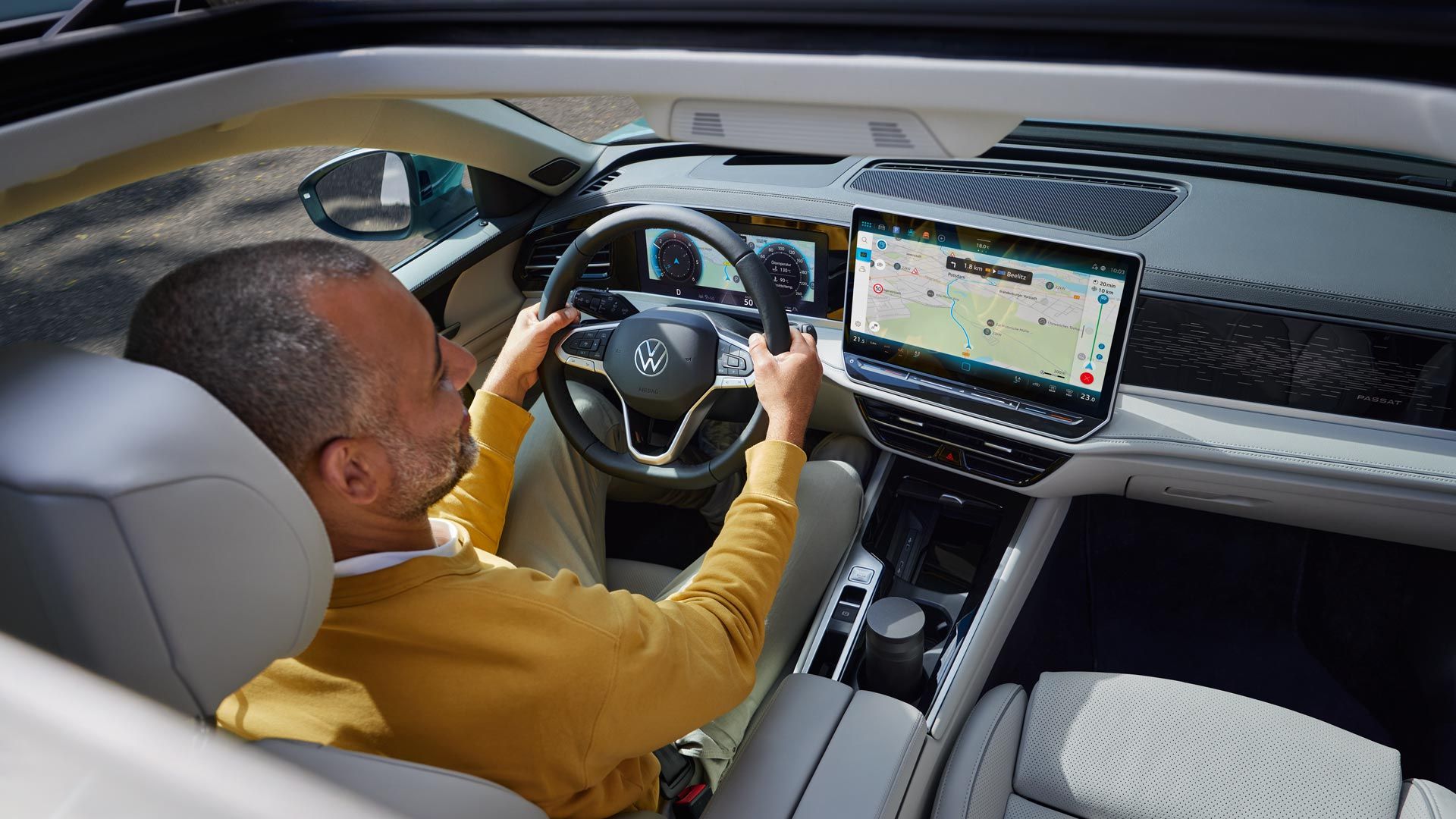Pohľad zhora cez otvorené voliteľné strešné okno VW Passat, kde muž sedí s oboma rukami na volante a pozerá sa na displej systému infotainment, kde je veľká navigačná mapa.