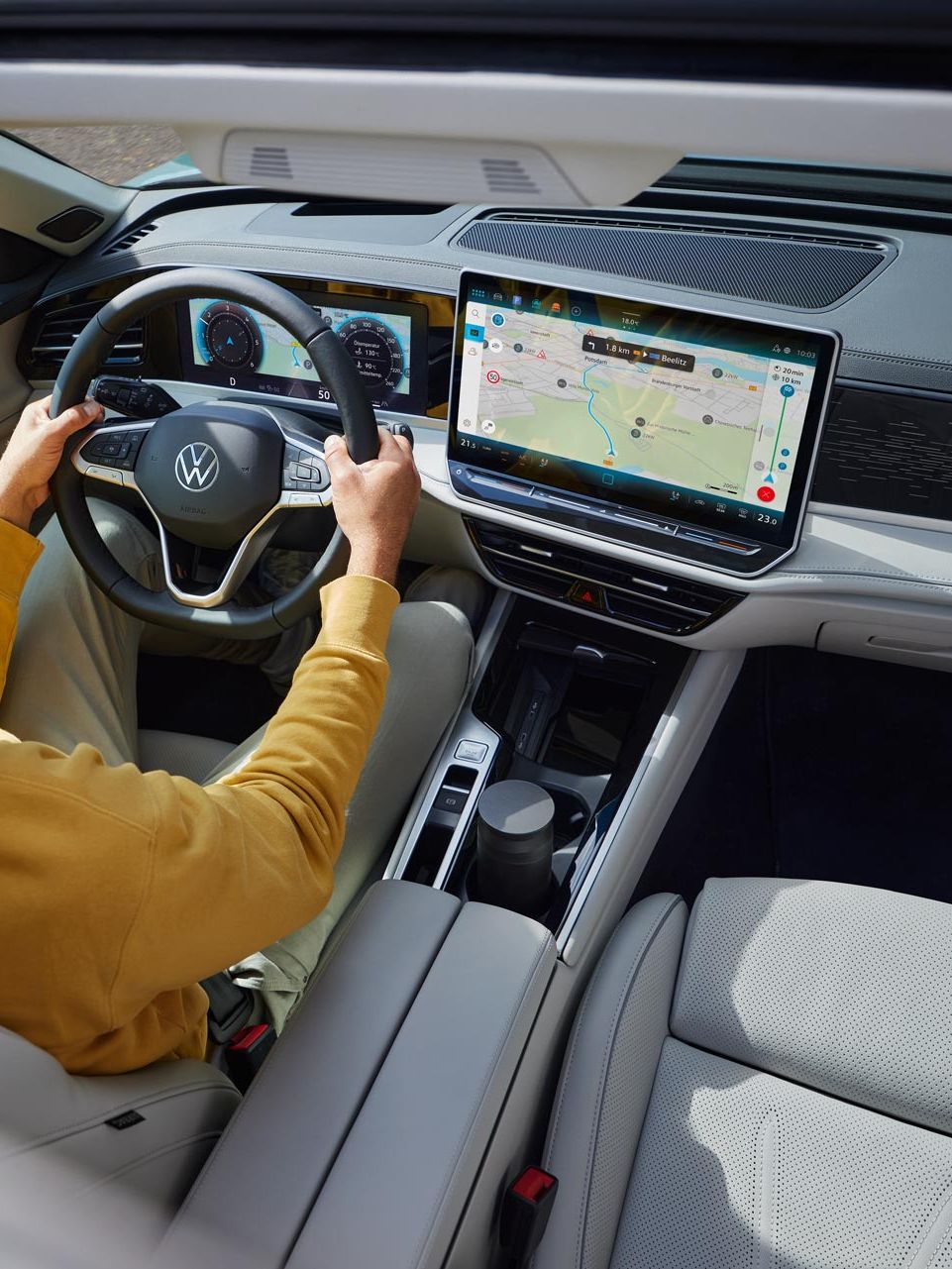 Pohľad zhora cez otvorené voliteľné strešné okno VW Passat, kde muž sedí s oboma rukami na volante a pozerá sa na displej systému infotainment, kde je veľká navigačná mapa.
