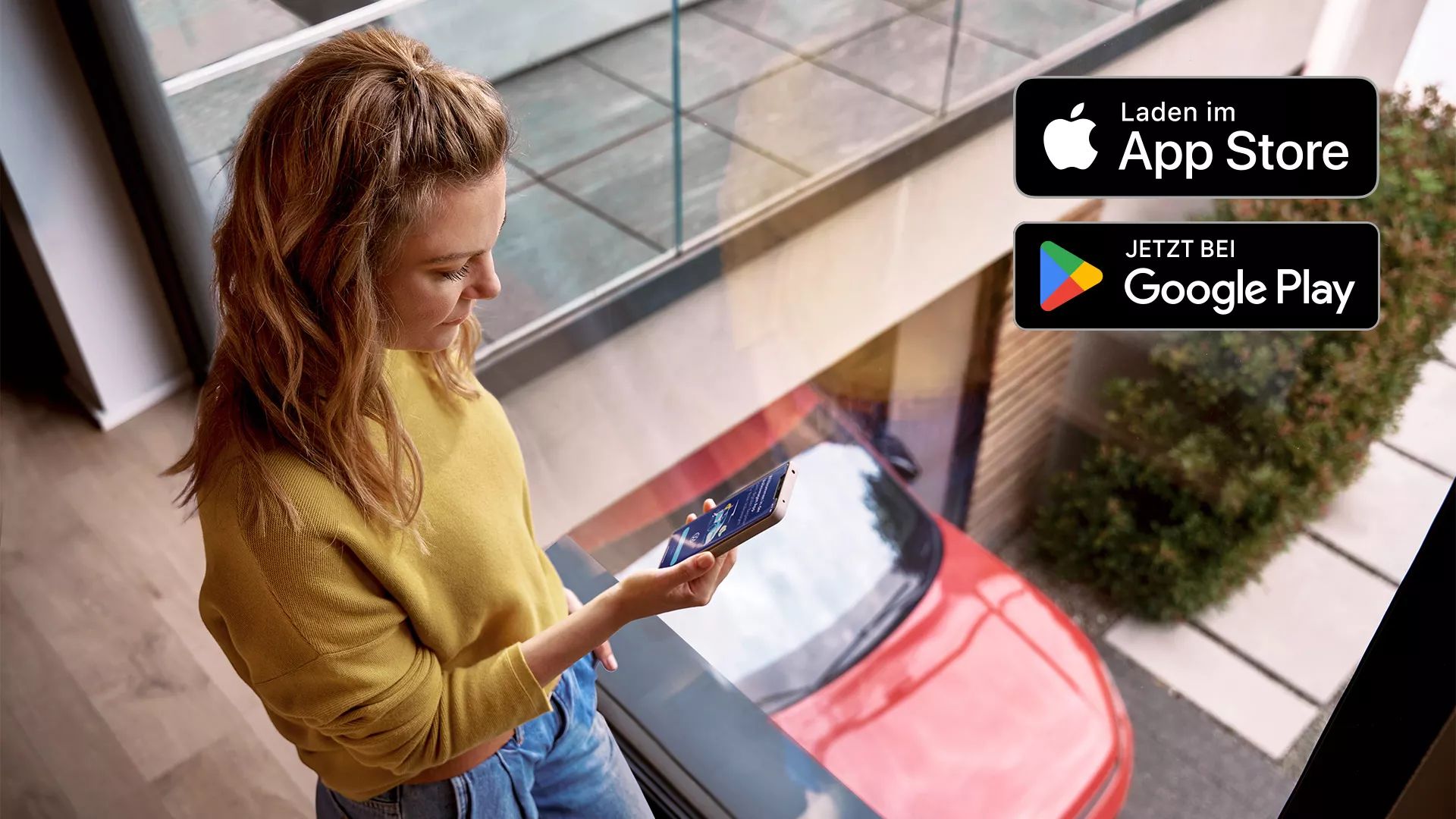 Žena sa pozerá na mobilný telefón. V pozadí je červený Volkswagen. V pravom hornom rohu sú logá obchodov App Store a Google Play Store.