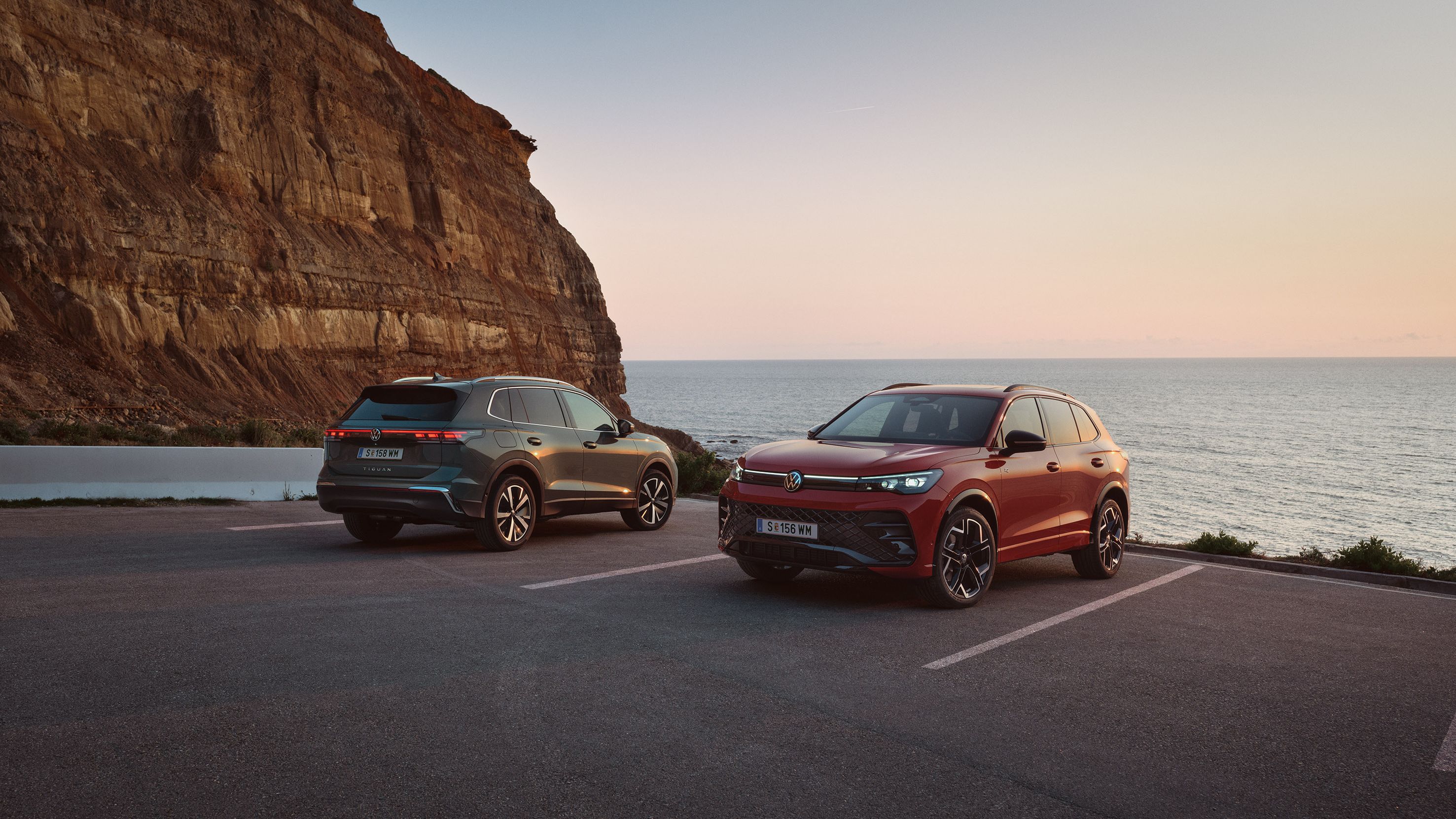 VW Tiguan v tmavozelenom a červonm odtieni parkujú pri pobreží pri skalnom útese.