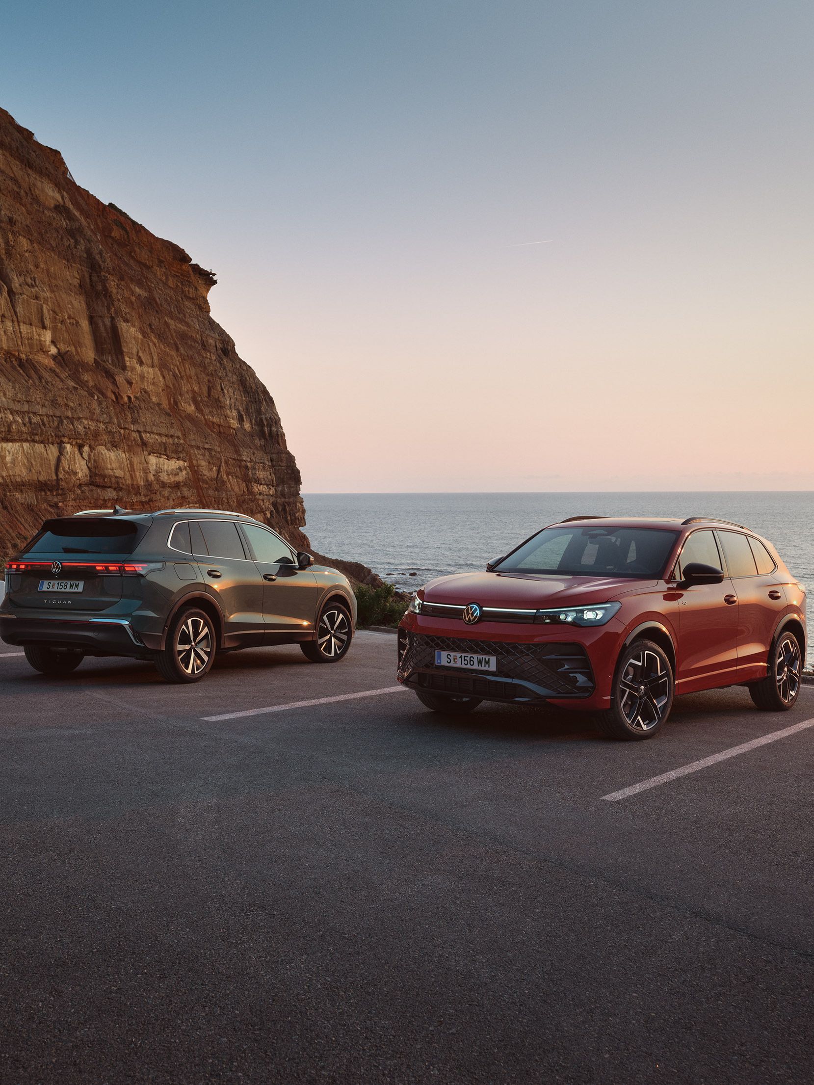 VW Tiguan v tmavozelenom a červonm odtieni parkujú pri pobreží pri skalnom útese.