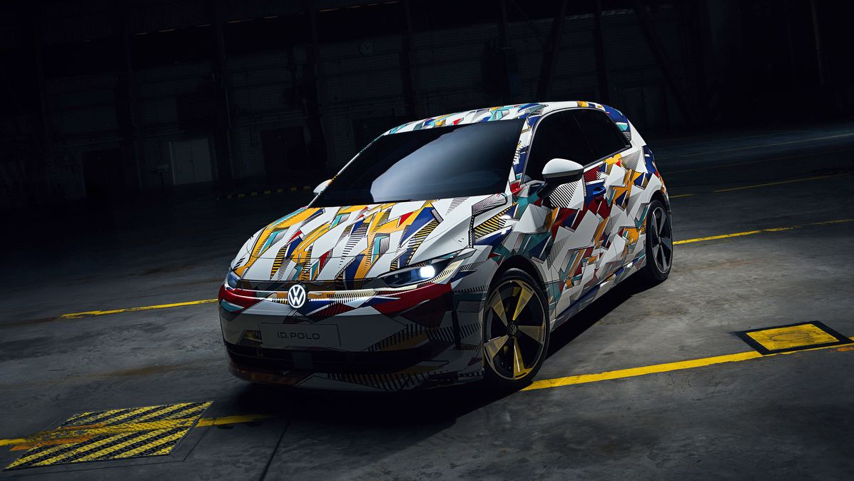 Malé mestské auto Volkswagen je na obrázku zaparkované v tmavej garáži. Vozidlo má pestrofarebne vzorovanú karosériu. Nad autom je veľká svetelná tabuľa, ktorá ho osvetľuje.