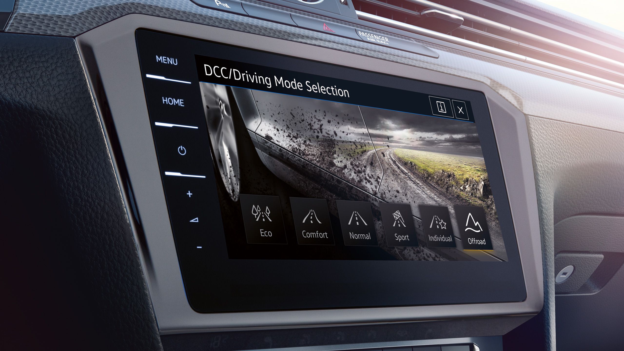 Dotykový displej automobilu s vybranými jazdnými režimami. Na displeji vidieť režimy Eco, Comfort, Normal, Sport, Individual a Offroad. Na pozadí je viditeľná zablatená cesta a krajina.