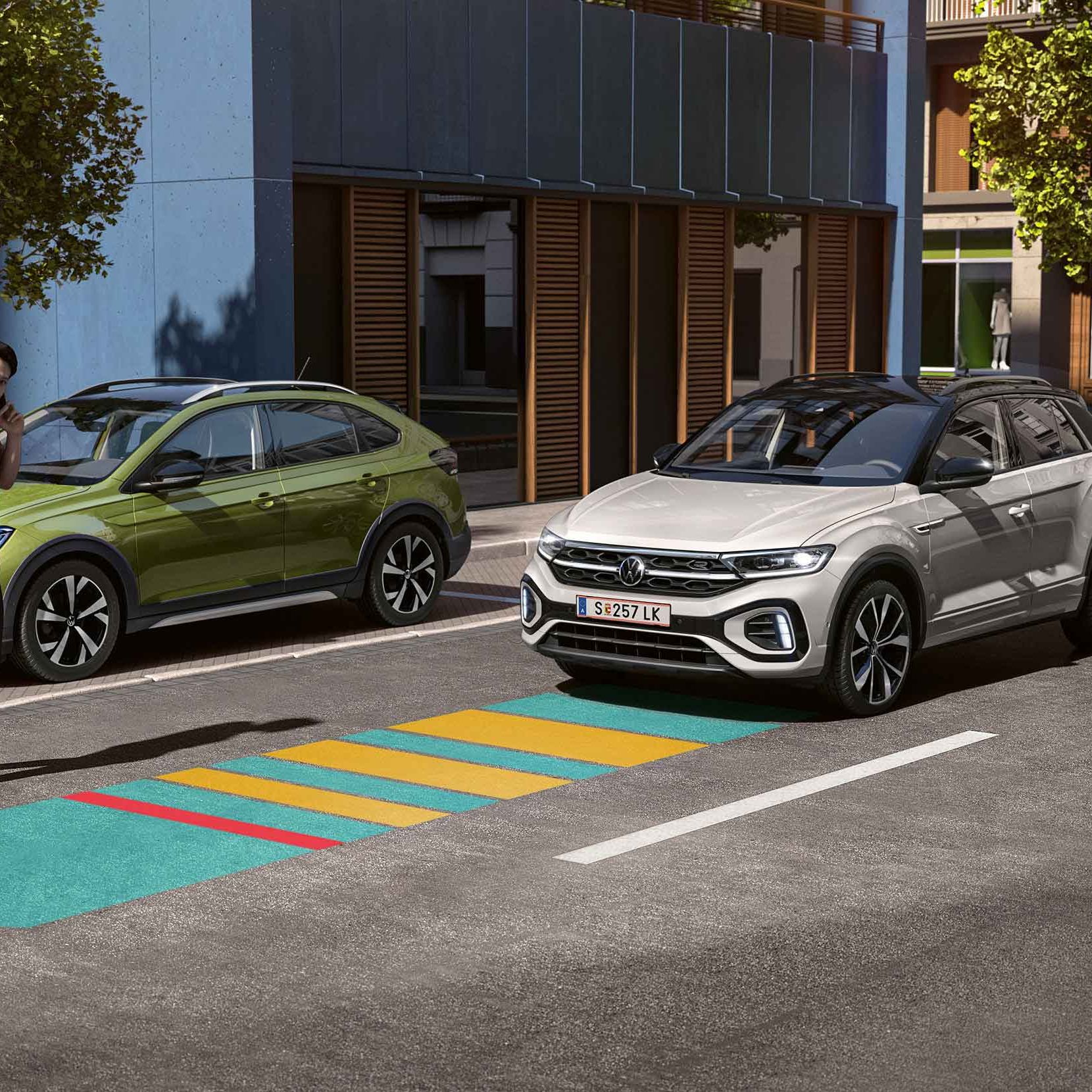 Grafika zobrazuje asistenta núdzového brzdenia Front Assist na modeli  VW T-Roc. Vozidlo jazdí po ceste v meste do cesty mu vchádza chlapec, ktorý telefonuje a nevníma vozidlo. Systém je znázornený modro-žlto-červenou líniou.