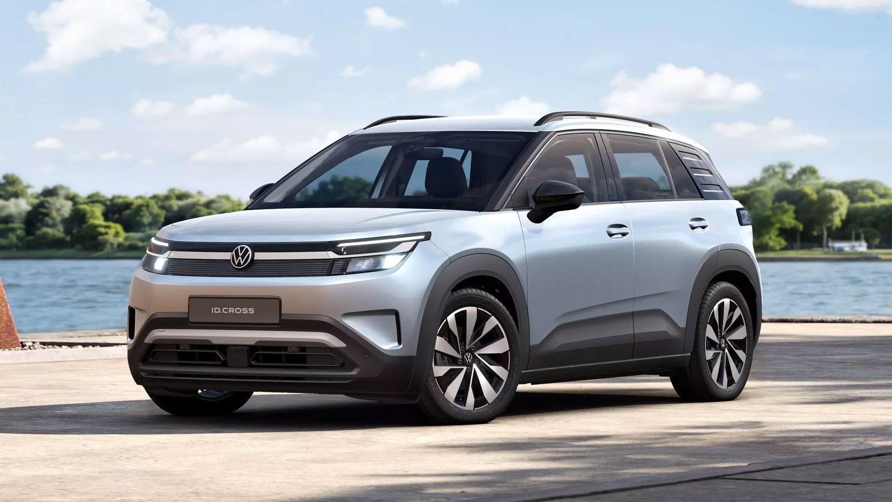 Strieborný VW ID. Cross Life s modernými, hranatými líniami stojí na betónovej ploche pri vodnej ploche. V pozadí sú vidieť stromy a mierne zamračenú oblohu. Vozidlo má futuristický dizajn.