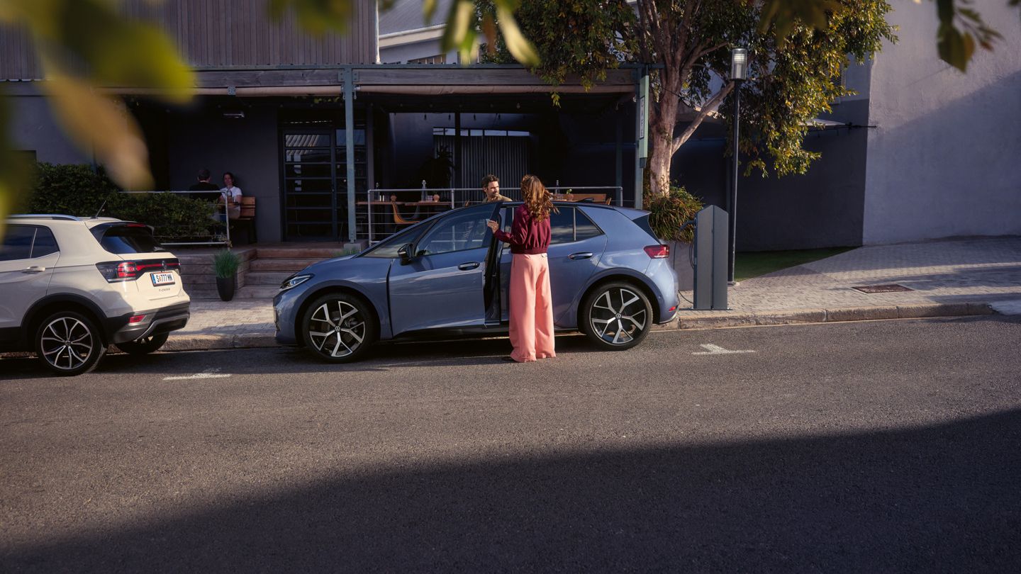 Žena a muž nastupujú do modrého VW ID.3 Neo, ktorý parkuje pred kaviarňou.