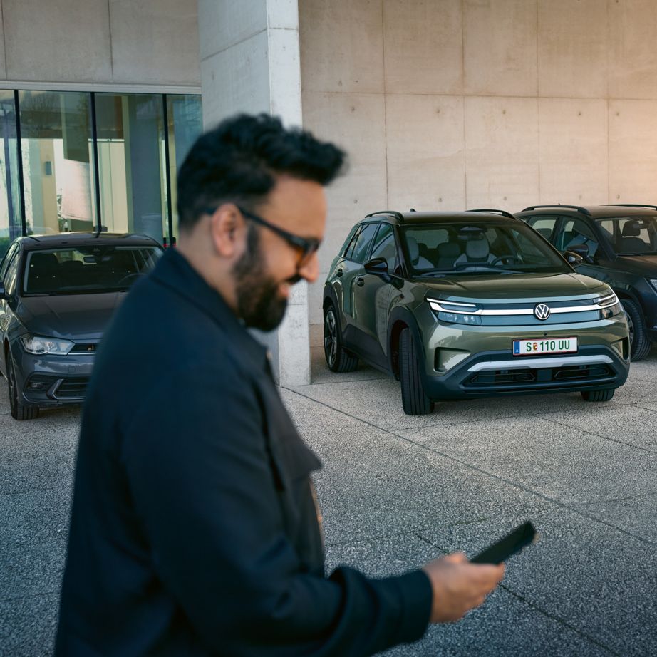 Muž sa pozrie na svoj smartfón, v pozadí VW ID. Cross automaticky zaparkuje na parkovacie miesto.