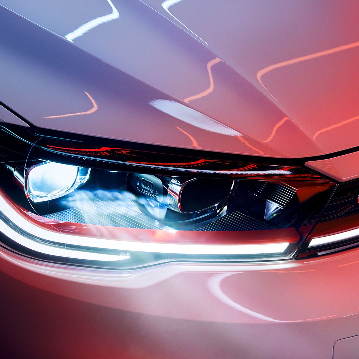 Detailný záber na predný svetlomet automobilu, s výrazným osvetlením a označením GTI. Svetlo má moderný dizajn s LED technológiou so svetelnými pásmi. Celý obraz je ladený do modro-červených tónov.