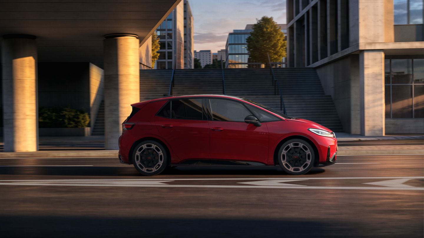 [AI-modified] – Červené VW ID.3 GTI z bočného pohľadu počas jazdy pod mostom v meste.
