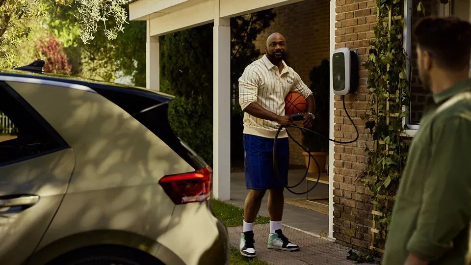 Muž sa rozpráva so svojím susedom a drží nabíjací kábel wallboxu. V popredí stojí Volkswagen ID.3