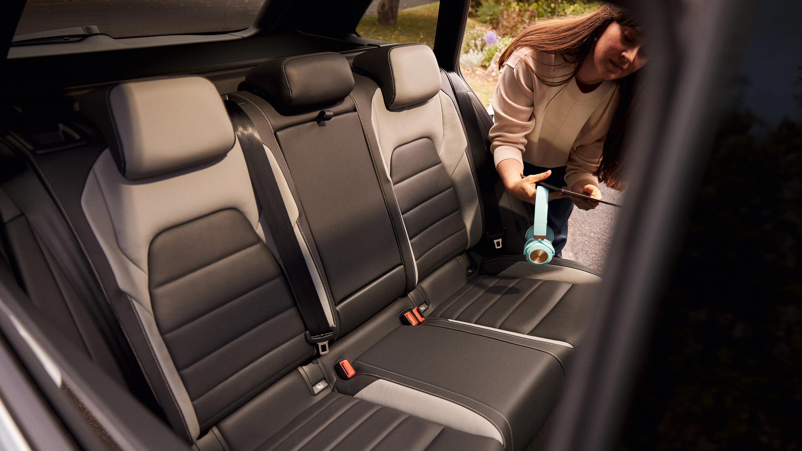 Pohľad na zadné sedadlo VW Golf Variant. Žena sa nakláňa do auta s otvorenými dverami, v ruke drží slúchadlá a tablet.