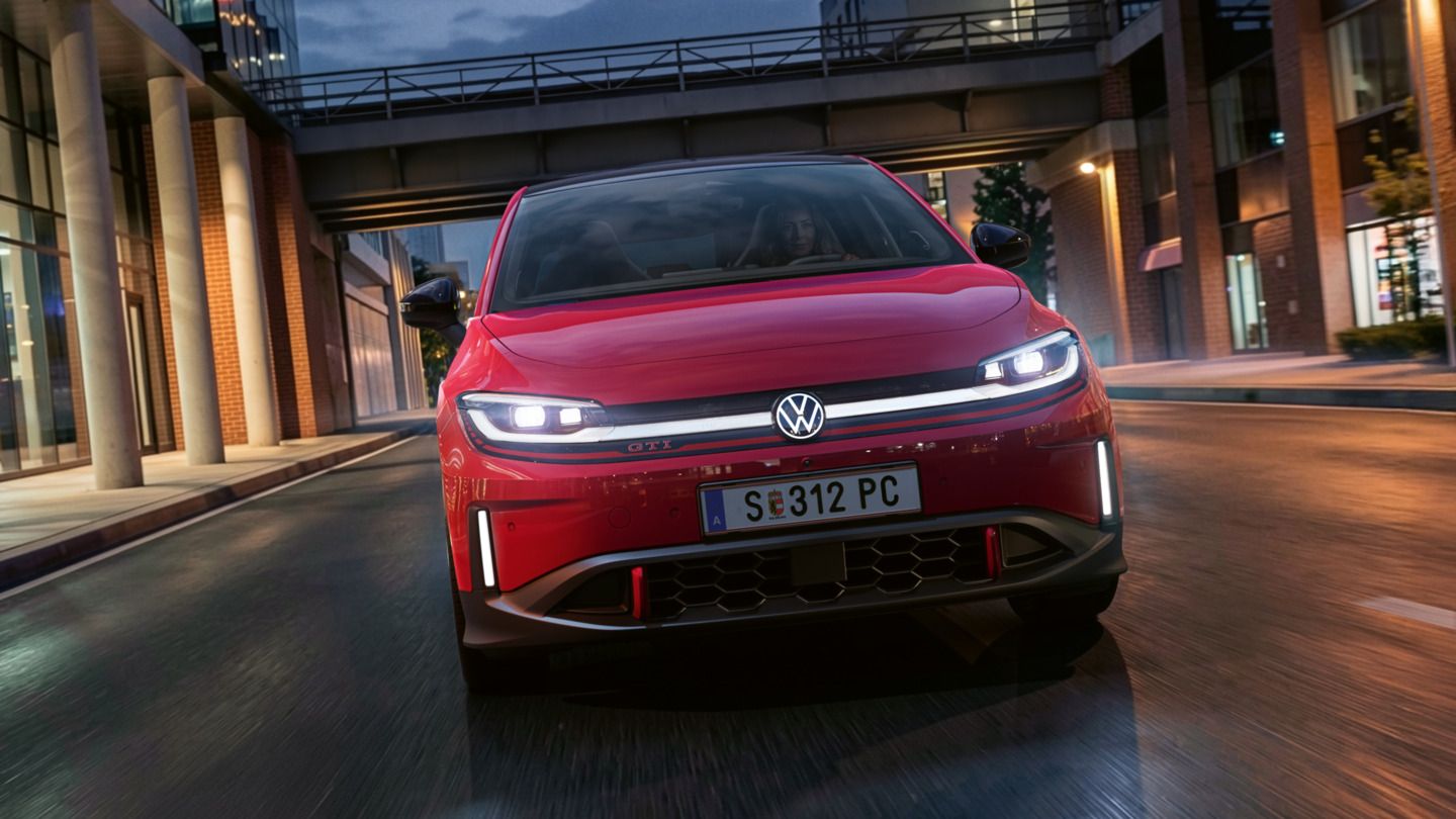Jedna osoba riadi červené VW ID. Polo GTI modernou osvetlenou obchodnou štvrťou večer.