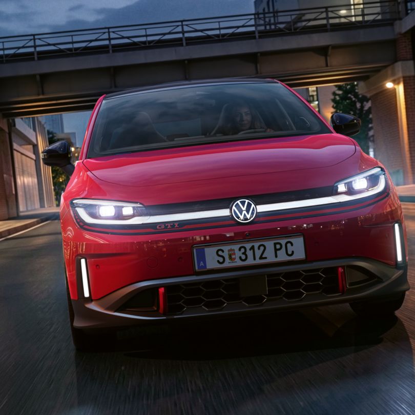 Jedna osoba riadi červené VW ID. Polo GTI modernou osvetlenou obchodnou štvrťou večer.