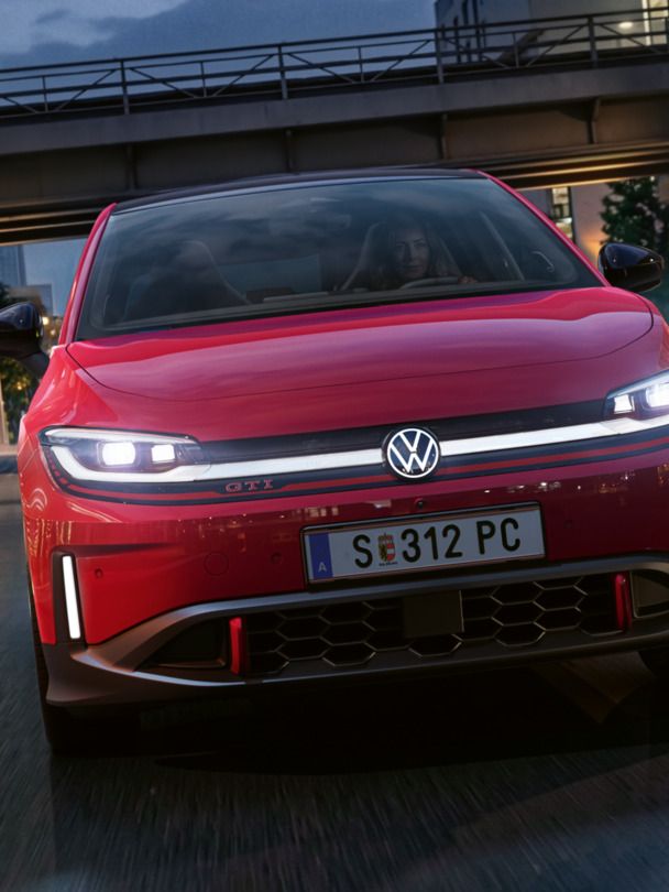 Jedna osoba riadi červené VW ID. Polo GTI modernou osvetlenou obchodnou štvrťou večer.