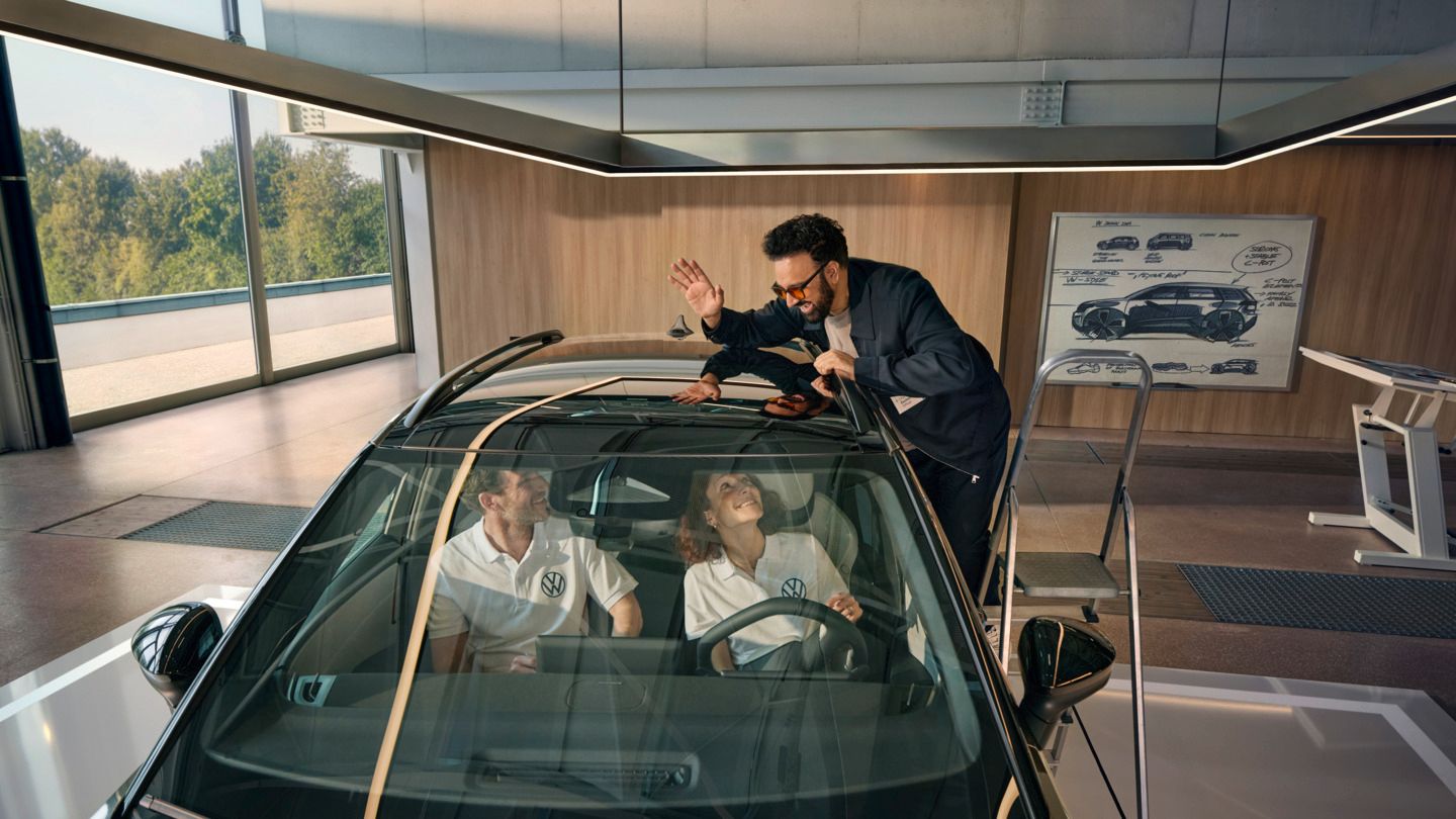 Muž stojí na rebríku vedľa vozidla VW ID. Cross a cez panoramatickú strechu máva ľuďom sediacim vo vnútri.