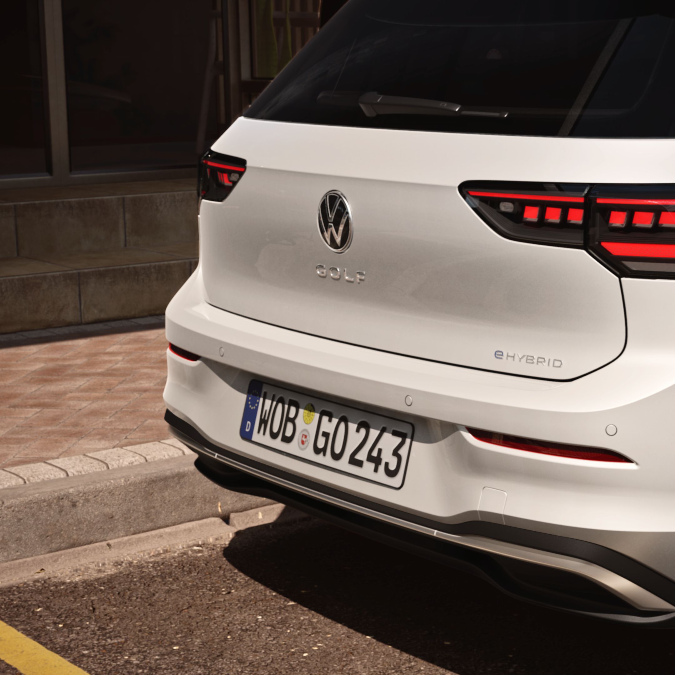 Biely Volkswagen Golf ehybrid stojí na parkovacom mieste. Obrázok sa zameriava na zadné partie vozidla s modernými zadnými LED svetlami, zadným nárazníkom logom VW a názvom modelu Golf. Na ľavej strane zadného nárazníka je umiestnený znak "eHYBRID".