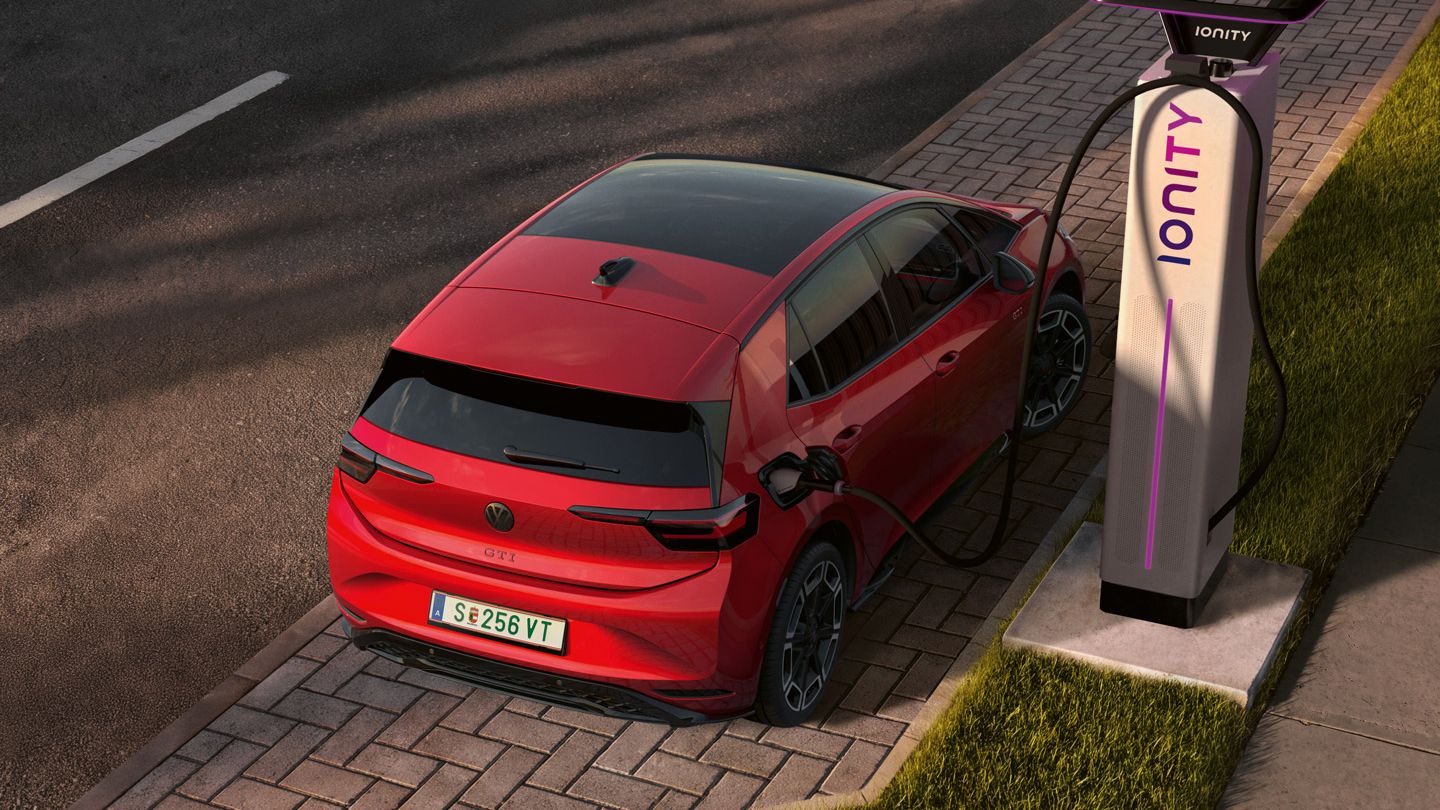 [AI-modified] – Pohľad šikmo zhora na ID.3 GTI, ktorý je pripojený k nabíjacej stanici na parkovacom mieste na okraji cesty.