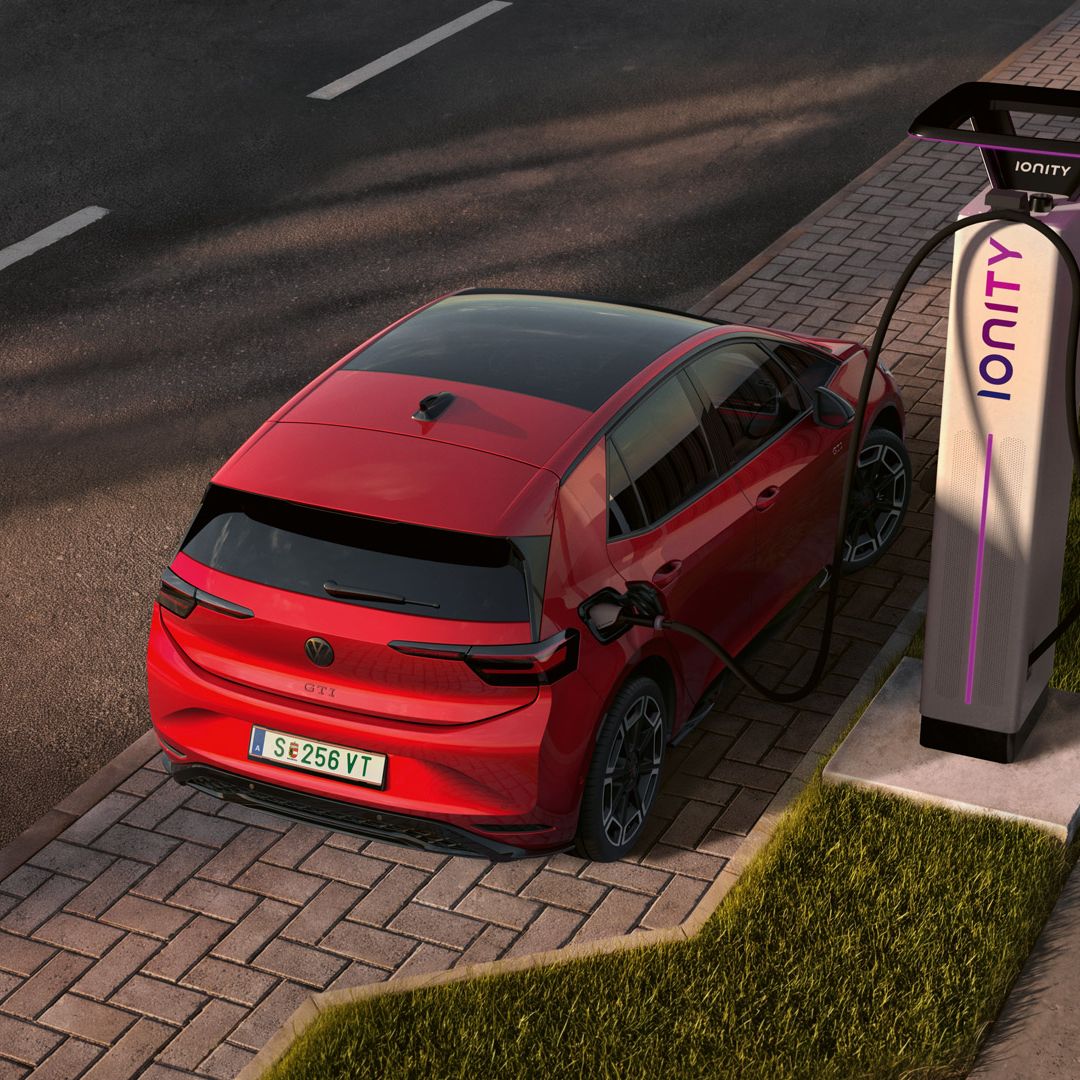 [AI-modified] – Pohľad šikmo zhora na ID.3 GTI, ktorý je pripojený k nabíjacej stanici na parkovacom mieste na okraji cesty.