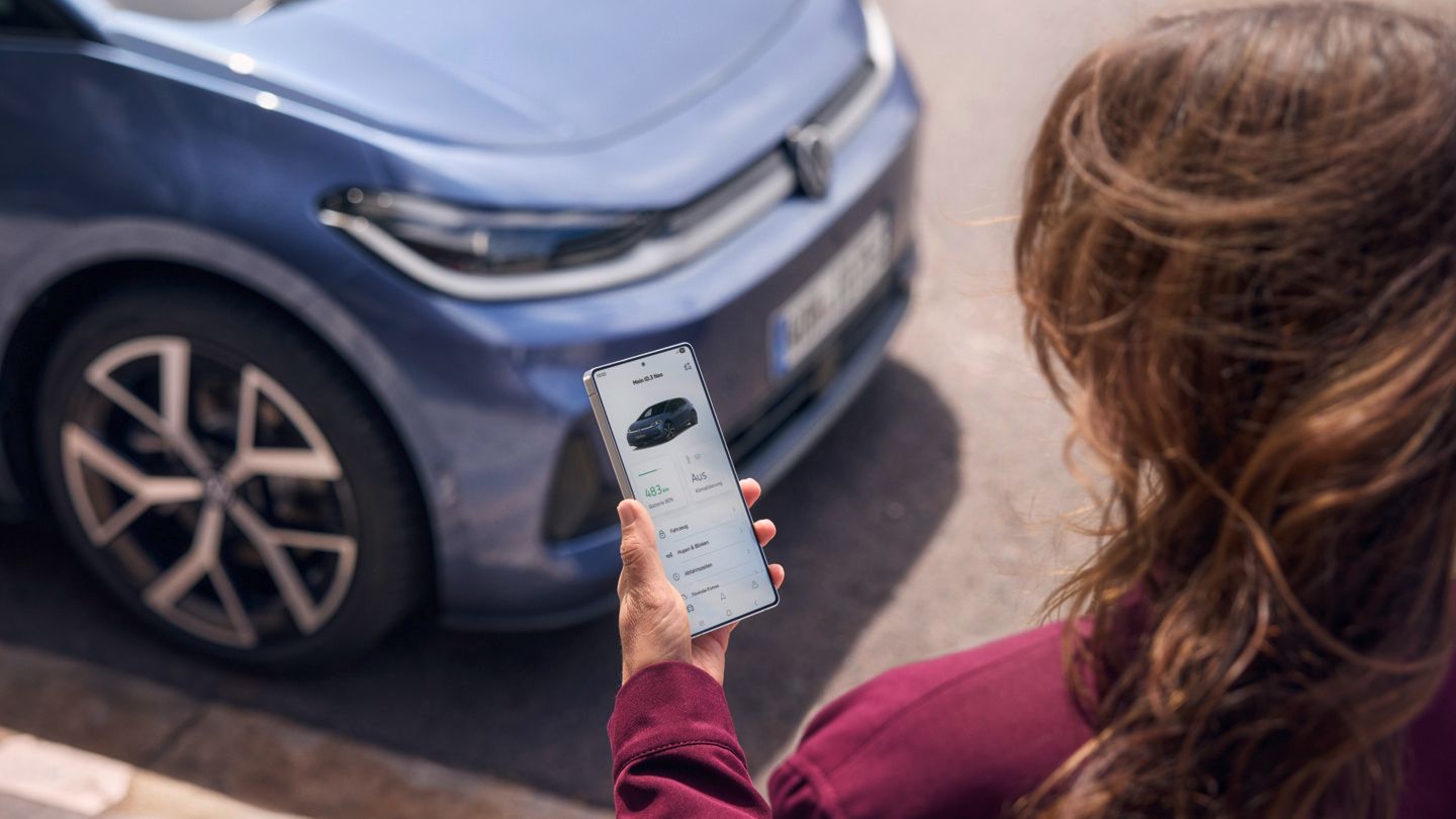 Žena sa pozerá na svoj smartfón, pred ňou stojí zaparkovaný modrý VW ID.3 Neo.