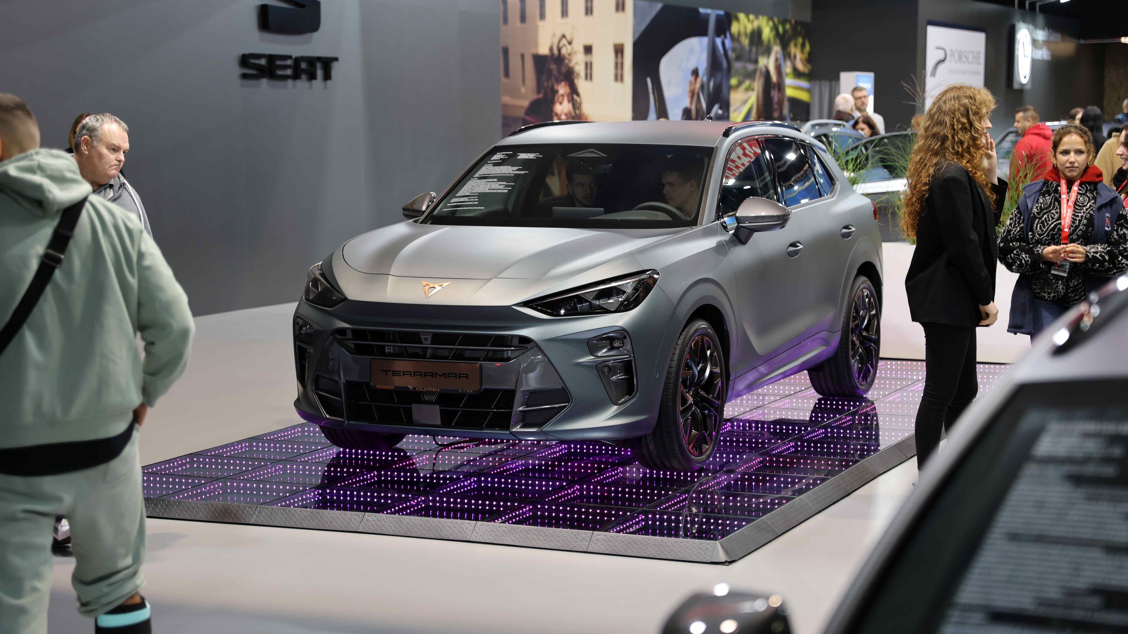 CUPRA Terramar vystavený na podstavci s osvetlením na autosalóne. Okolo stojí niekoľko ľudí, ktorí si vozidlo prezerajú. Na stene v pozadí je značka "SEAT".