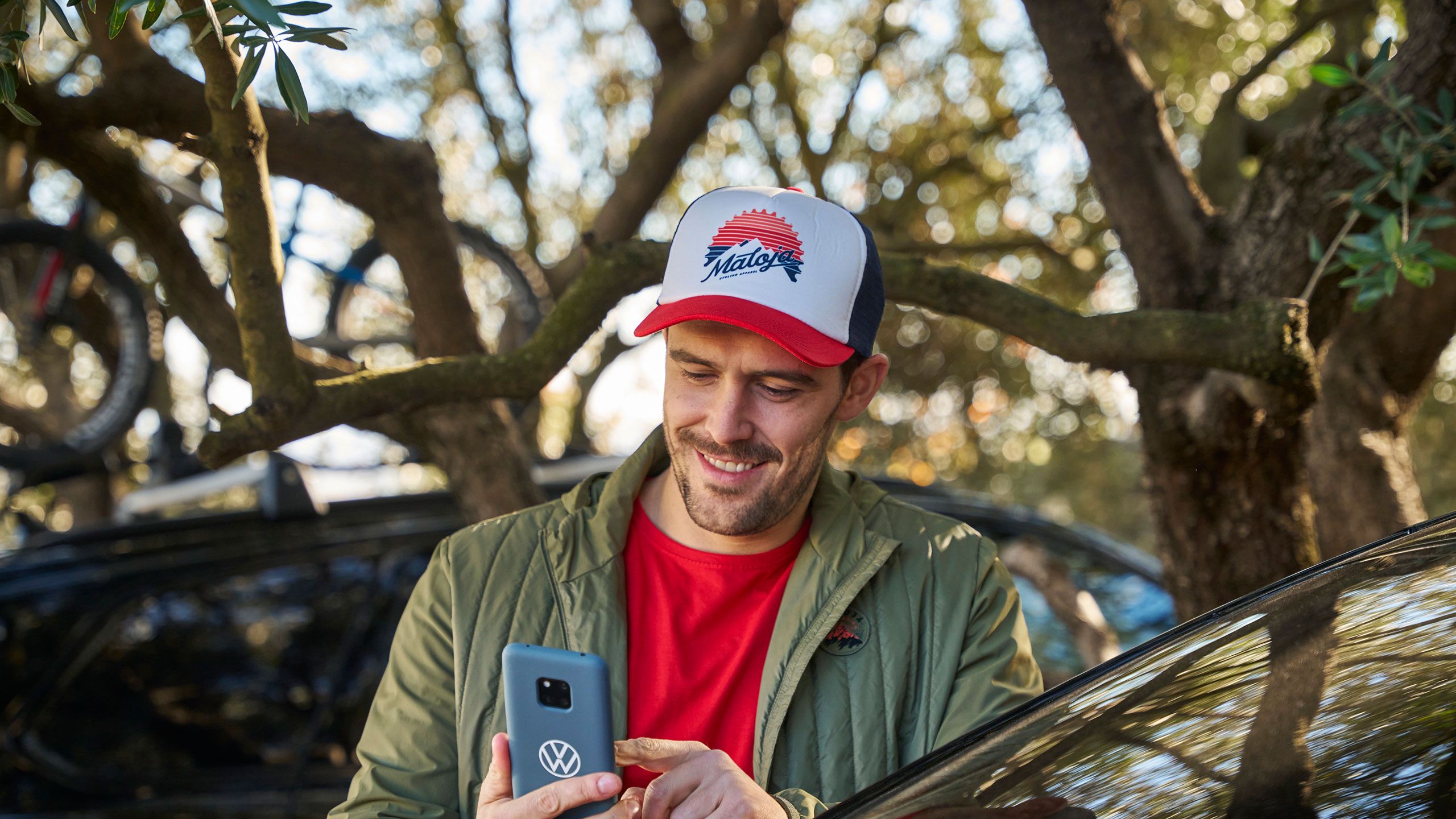 Muž s čiapkou sa pozerá na smartfón, vedľa neho vozidlo VW ID.