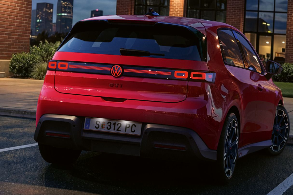 Pohľad na zadnú časť červeného VW ID. Polo GTI so zapnutými zadnými svetlami a osvetleným logom, ktoré parkuje pred administratívnou budovou.