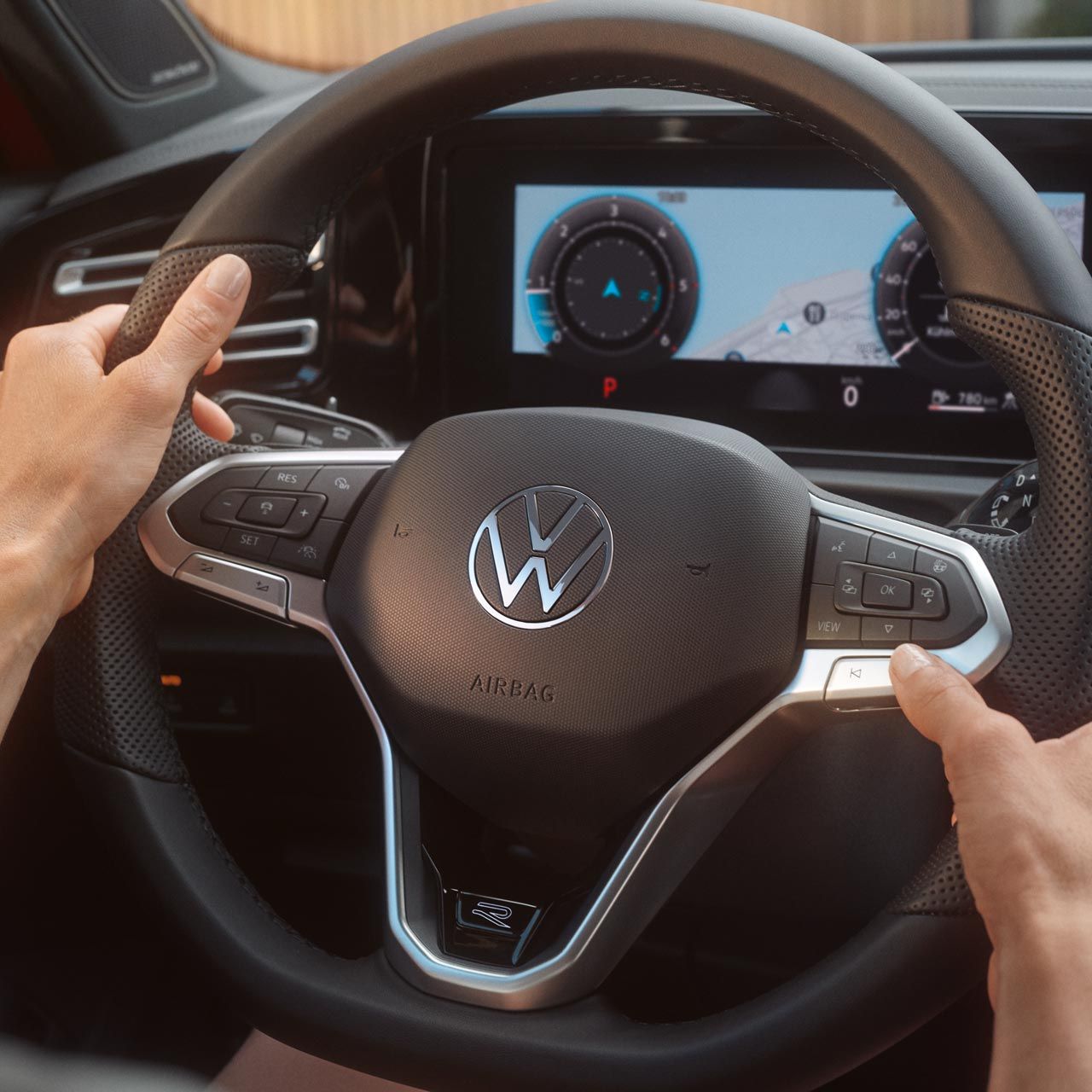 Ruky držia volant vozidla Volkswagen. Na digitálnom prístrojovom paneli je viditeľný displej so zobrazením navigácie a prístrojov. Na volante sú ovládacie tlačidlá.