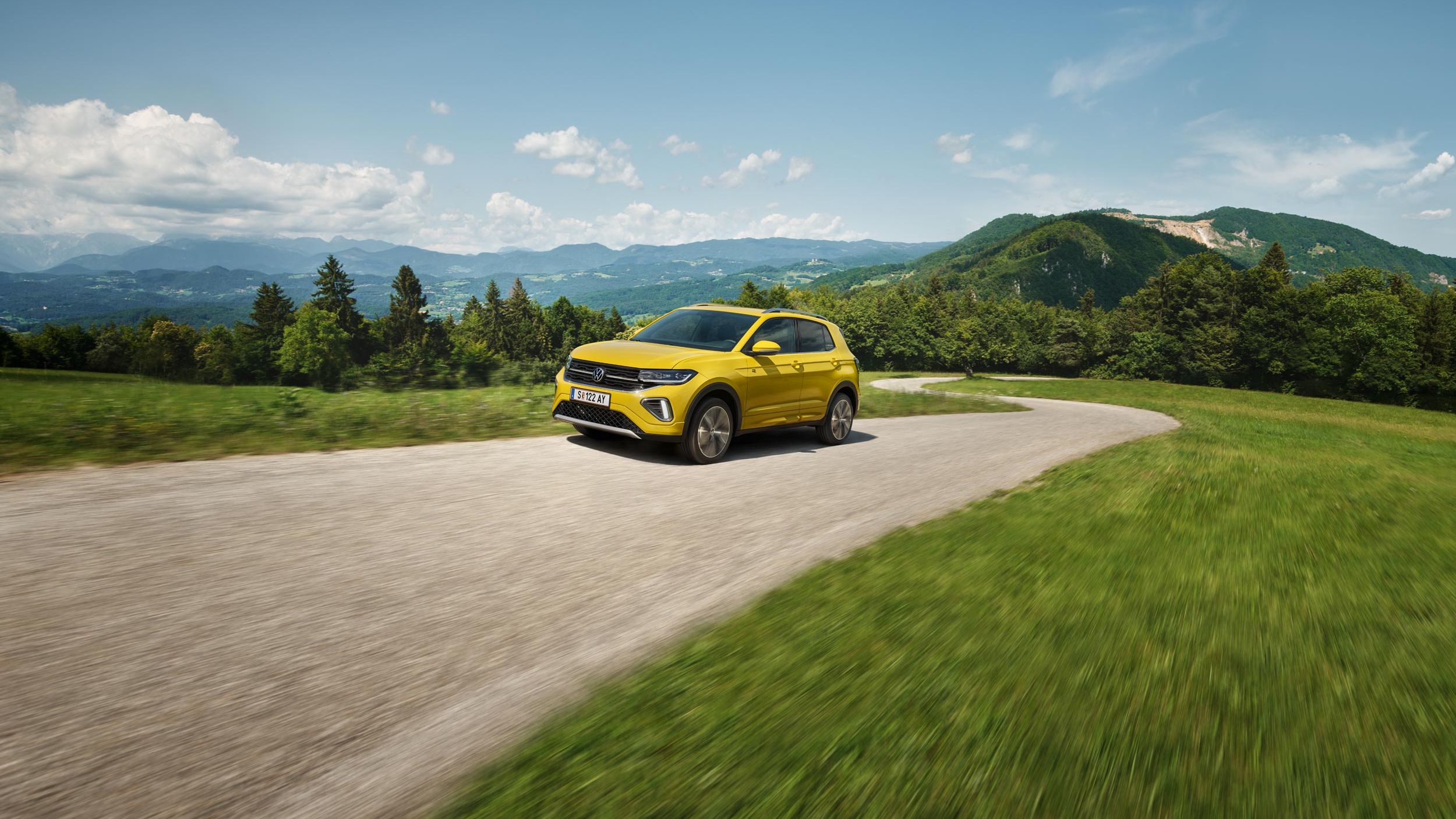 Žltý VW T-Cross na ceste v hornatej krajine.