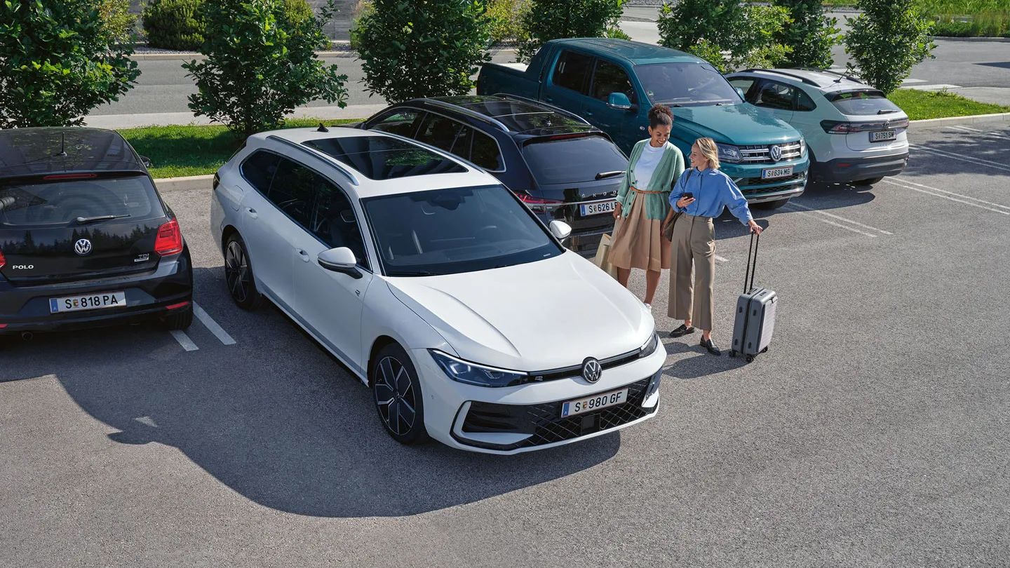 VW Passat stojí na parkovisku, vedľa neho sú dve osoby s batožinou.