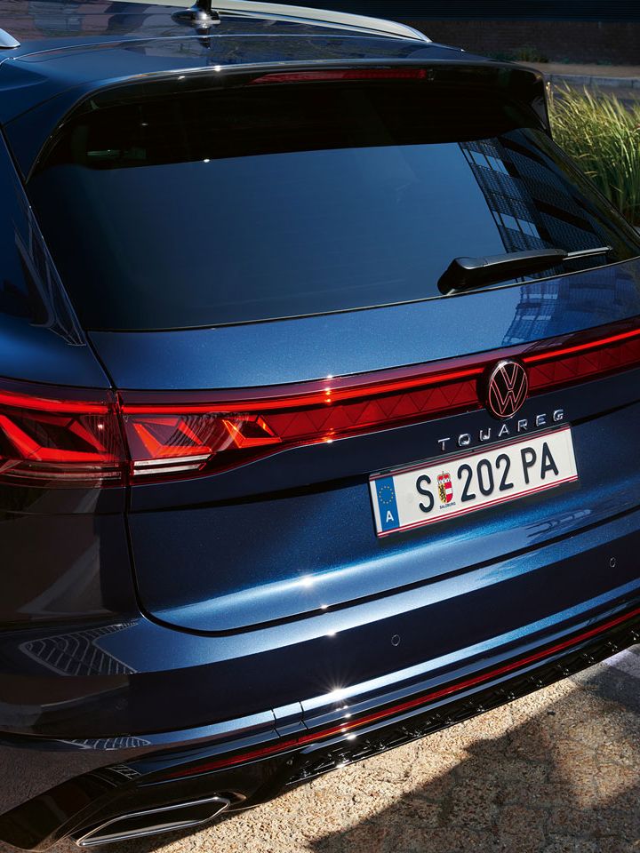 Pohľad na zadné partie modrého Volkswagen Touareg. Auto je zaparkované na parkovacom mieste pri ceste v meste. V pozadí vidieť pás zelene a chodník.
