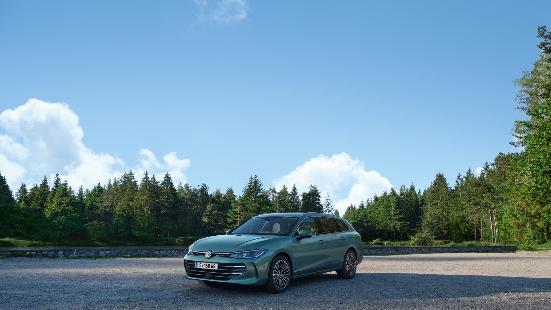 Zelený VW Passat je zaparkovaný na štrkovom priestore v lese. Atmosféru dotvára modrá obloha. Automobil je typu kombi. Scéna je pokojná a slnečná.