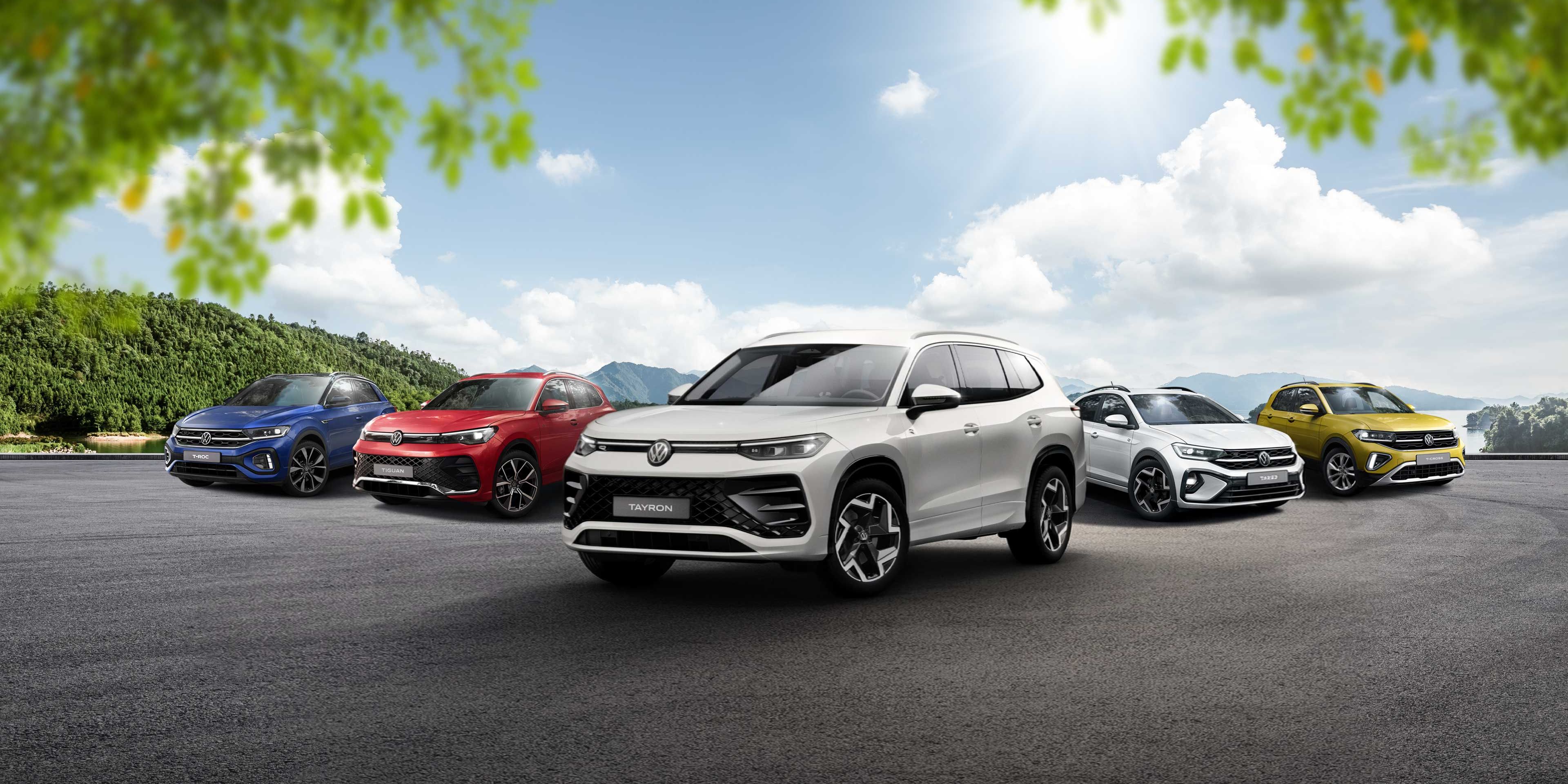 Päť rôznych vozidiel Volkswagen rôznych modelov a farieb zaparkovaných na otvorenom priestranstve. Automobil v popredí je veľké biele SUV. Okolie tvorí modrá obloha s oblakmi a stromy.