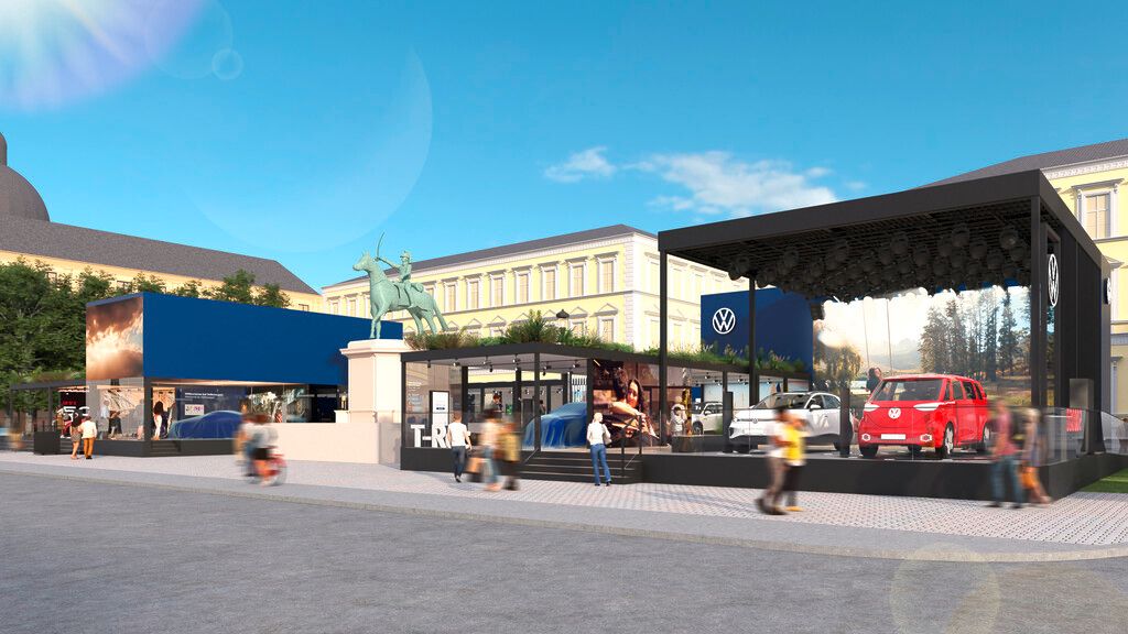 Vonkajšia výstava automobilov značky Volkswagen, vrátane modelov SUV. Na výstave sú okrem áut aj propagačné stánky spoločnosti Volkswagen. Pozadie tvoria historické budovy pod jasnou oblohou.