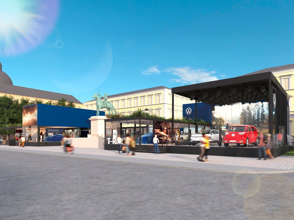 Vonkajšia výstava automobilov značky Volkswagen, vrátane modelov SUV. Na výstave sú okrem áut aj propagačné stánky spoločnosti Volkswagen. Pozadie tvoria historické budovy pod jasnou oblohou.
