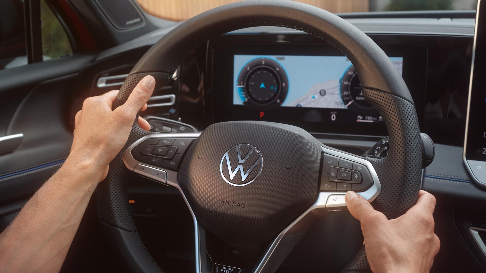 Ruky držia volant vozidla Volkswagen. Na digitálnom prístrojovom paneli je viditeľný displej so zobrazením navigácie a prístrojov. Na volante sú ovládacie tlačidlá.